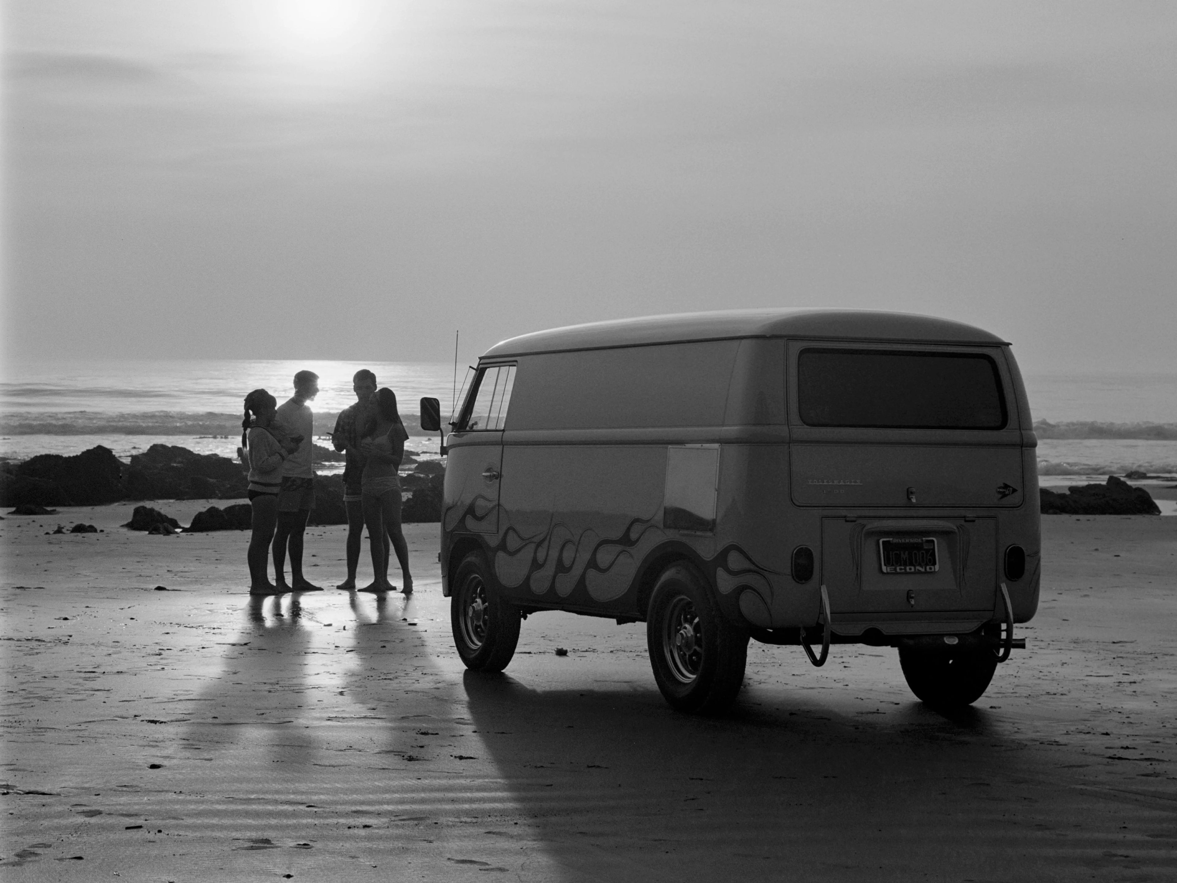 Un grupo de jóvenes surfistas y su US Rubber VW Volkswagen Bus personalizada durante la puesta de sol en una playa del sur de California en 1967.