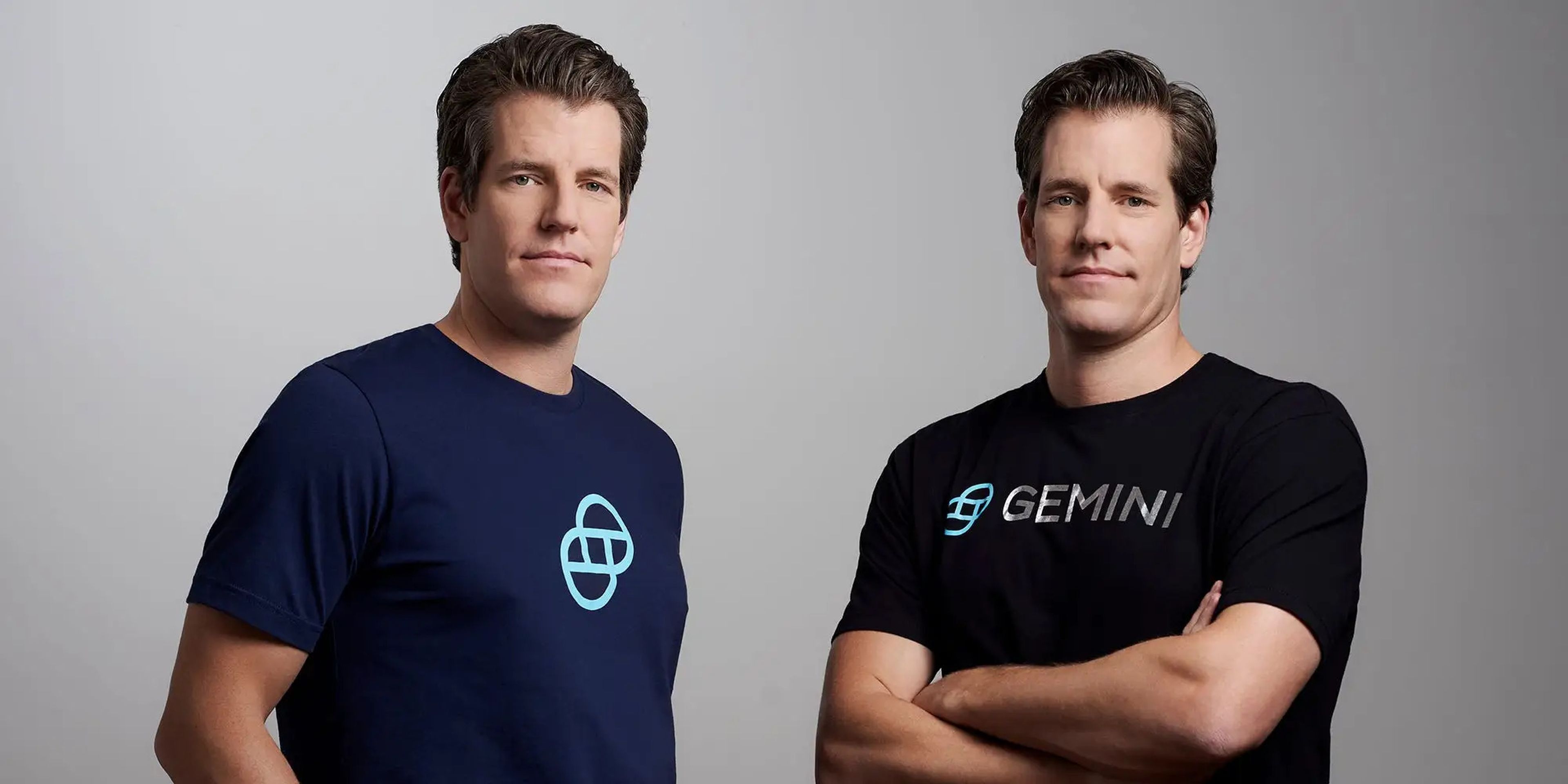 Gemini cofounders Tyler and Cameron Winklevoss pose for a photo against a gray background.