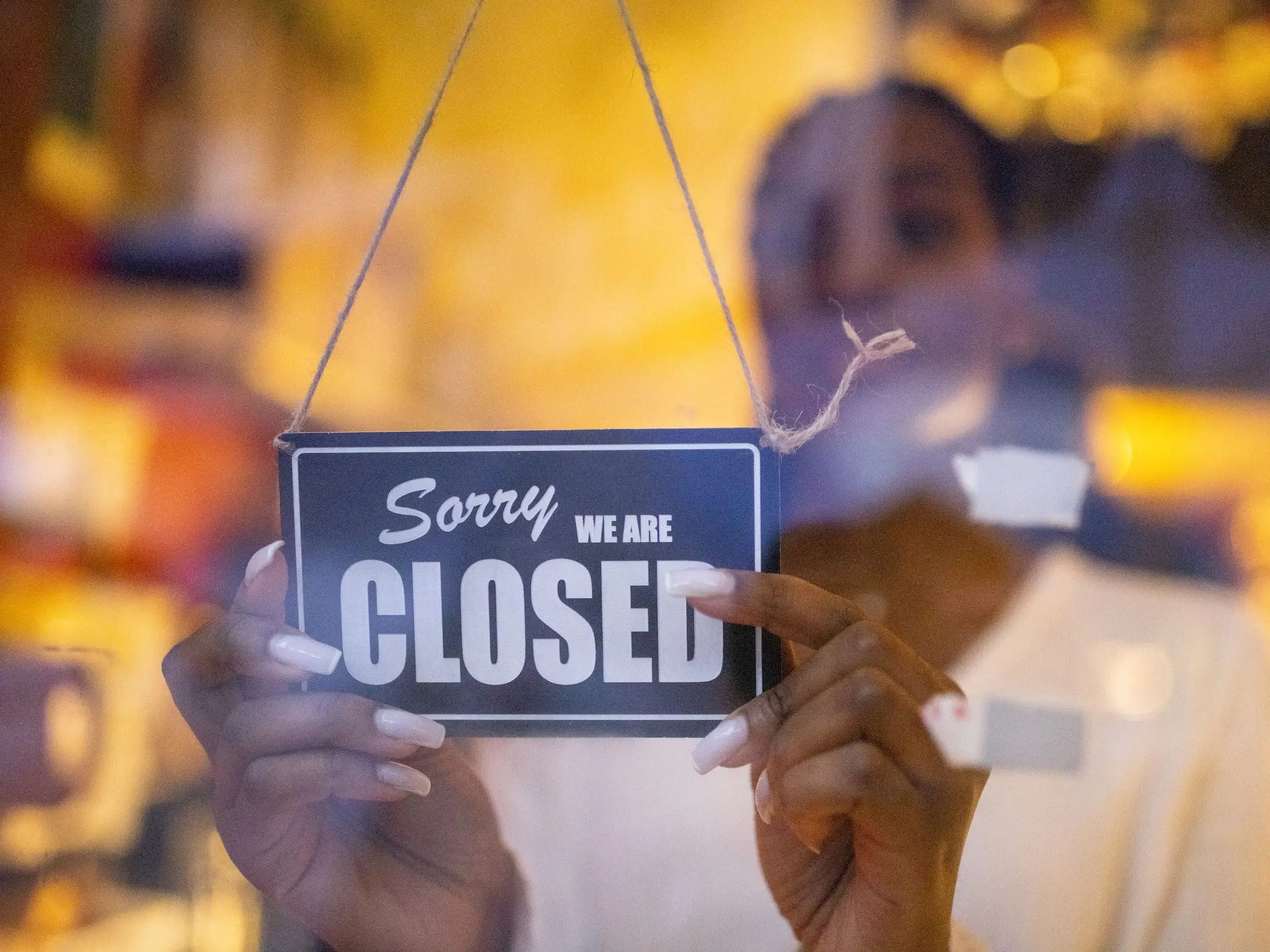 Una mujer pone un cartel de cerrado en la puerta de cristal de una cafetería. 