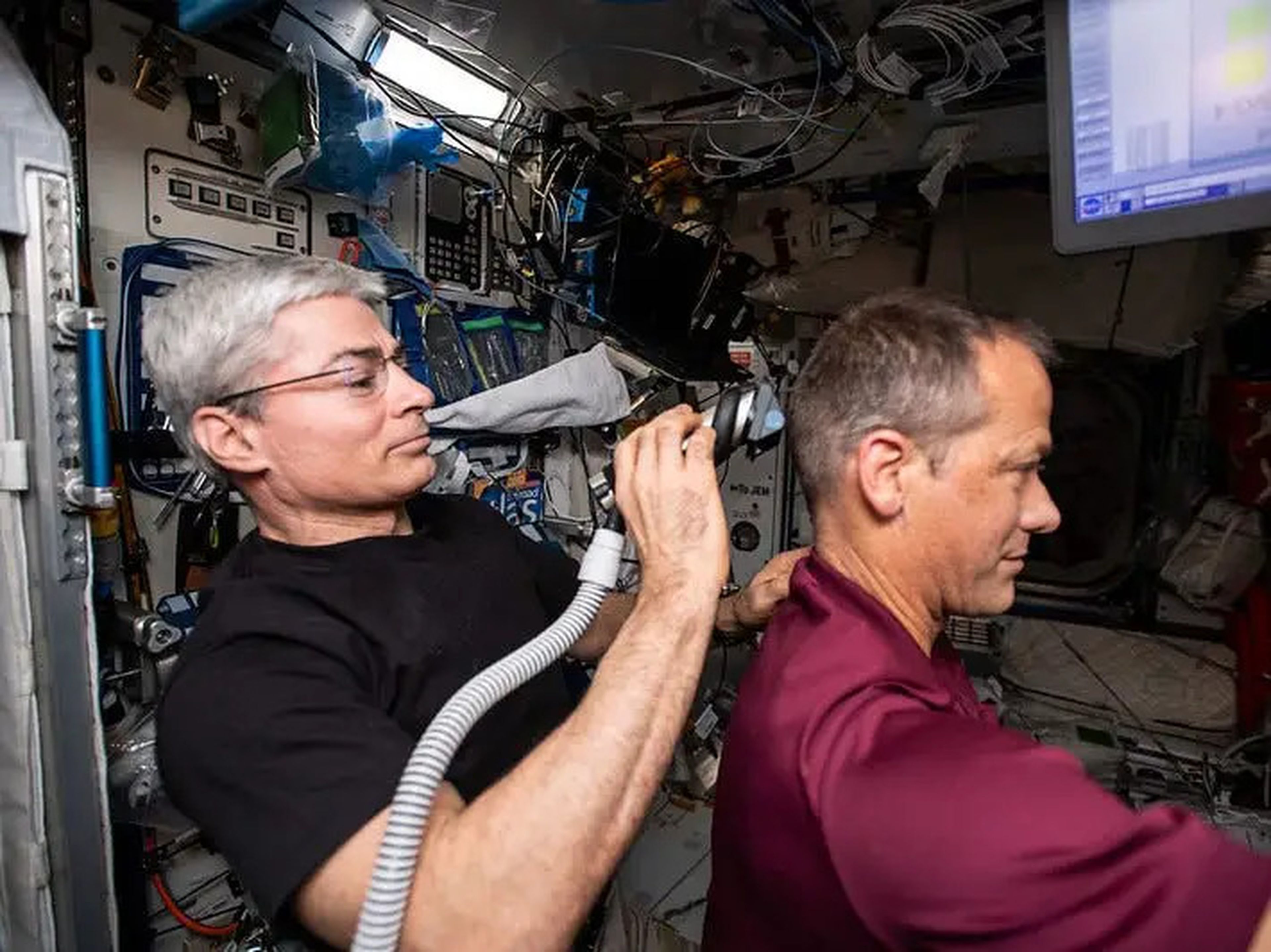 Vande Hei usa una maquinilla de afeitar eléctrica con una aspiradora que recoge el cabello que está cortando a su compañero astronauta de la NASA, Thomas Marshburn.