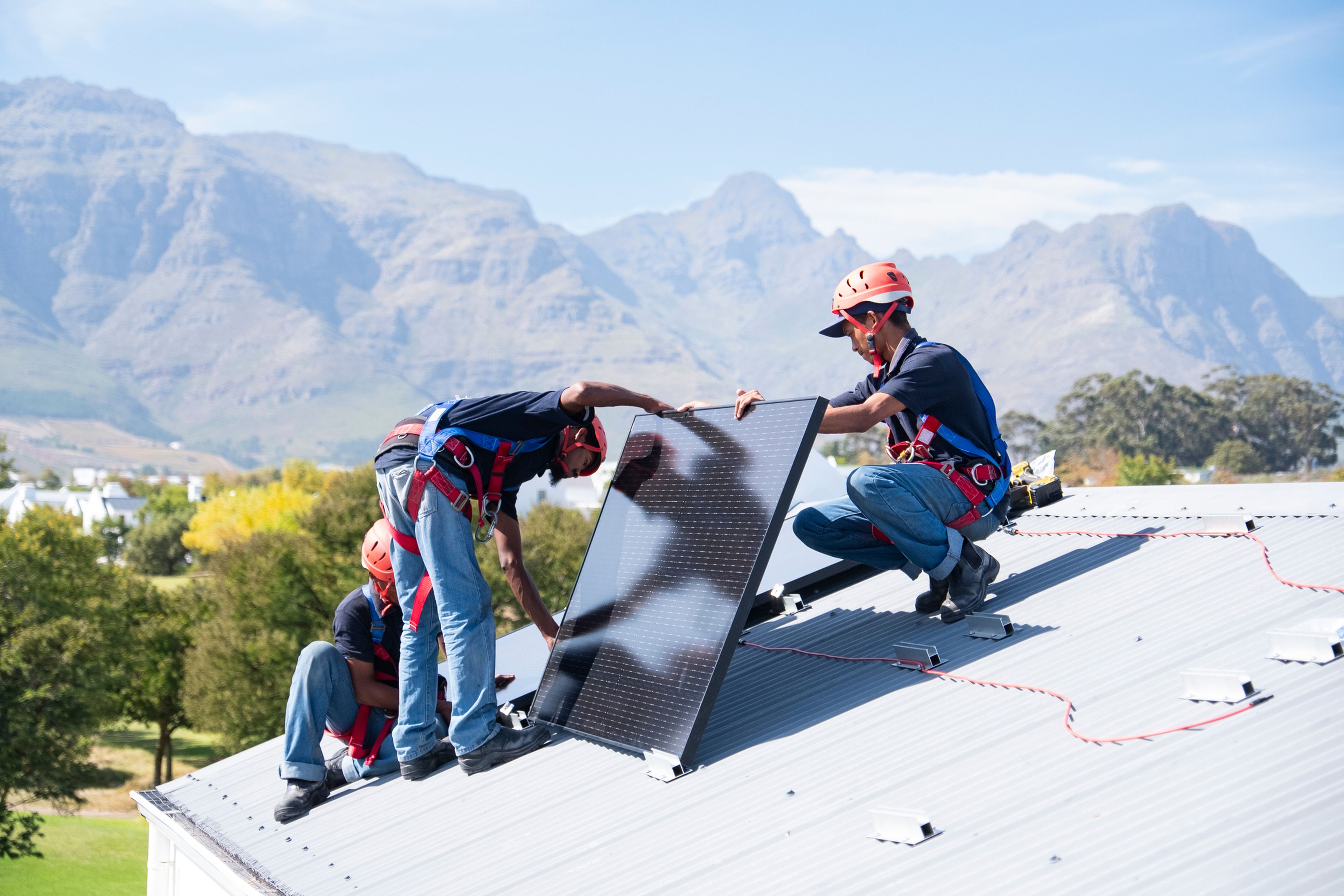 Varias personas instalan placas solares en un tejado.