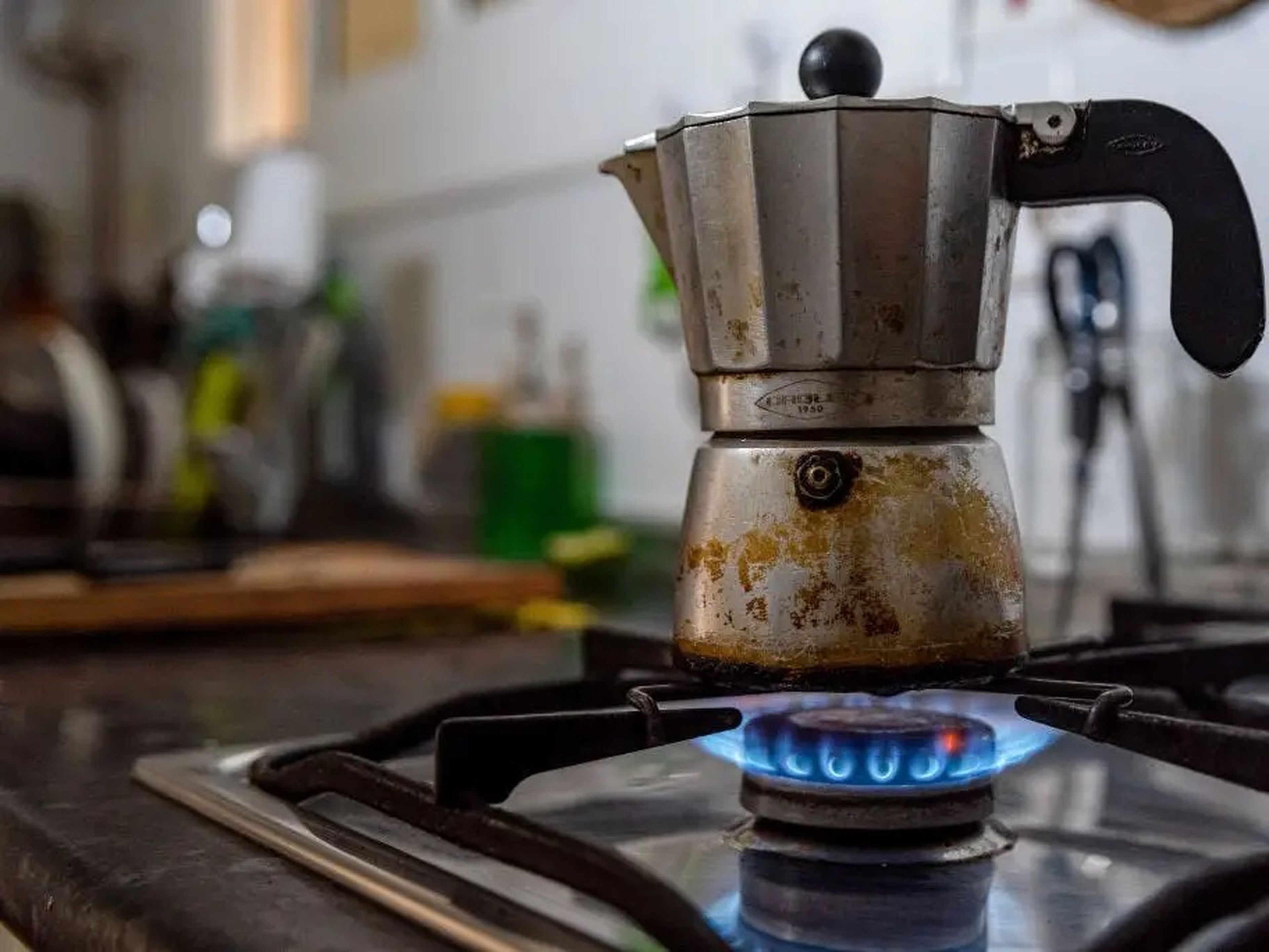 A coffee pot is seen over a blue flame gas stove inside a kitchen