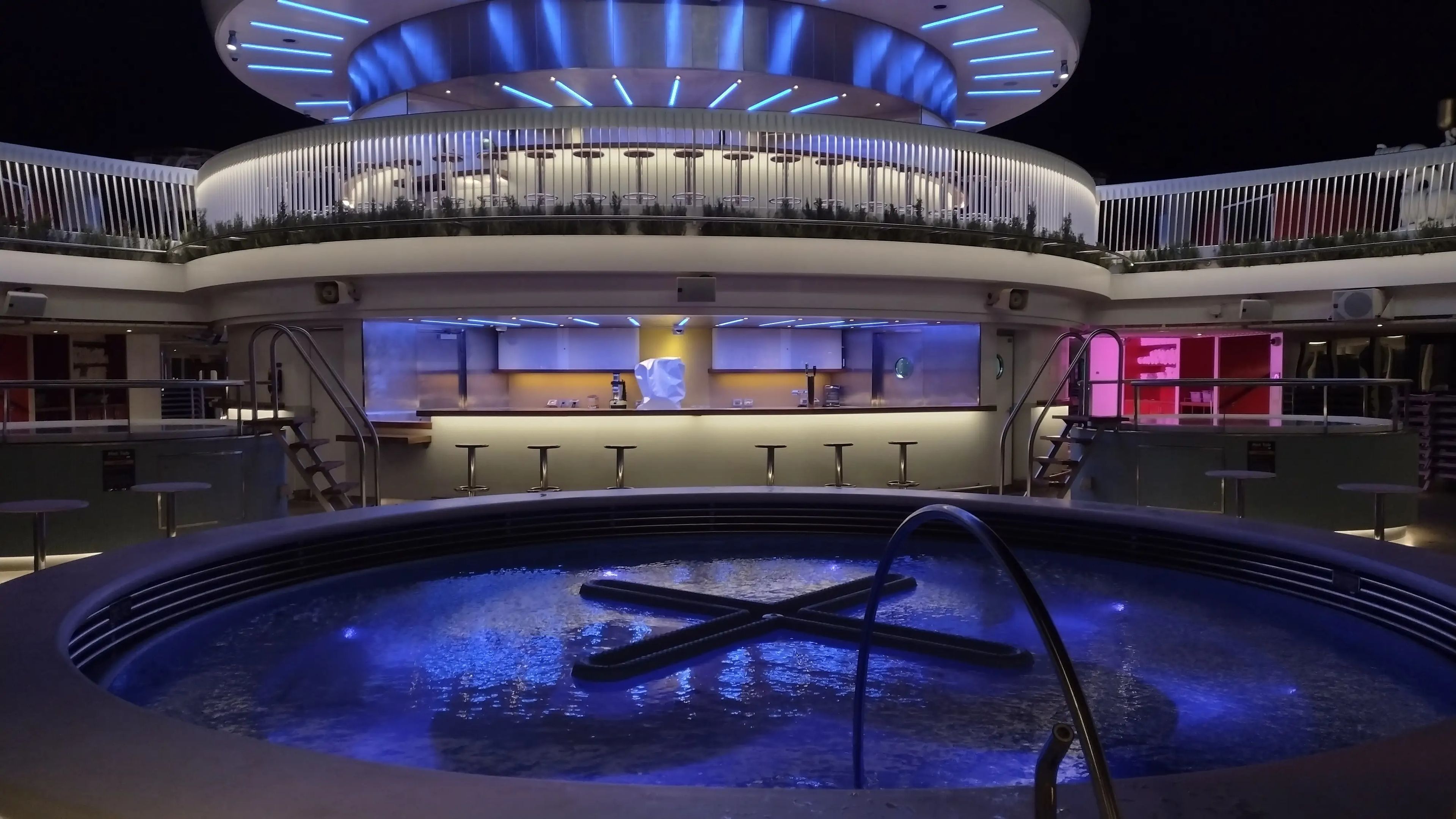 A cruise ship pool lit up at night with purple lights.