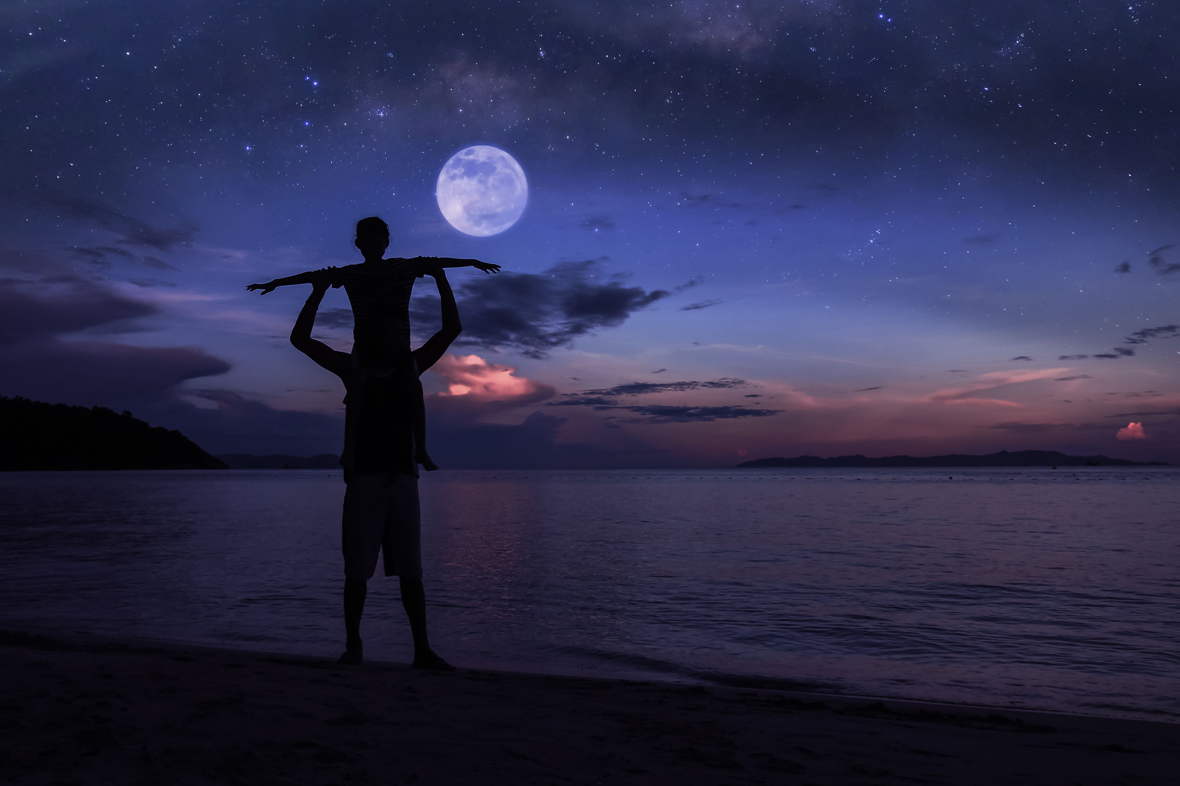 Dos personas mirando la luna en la playa