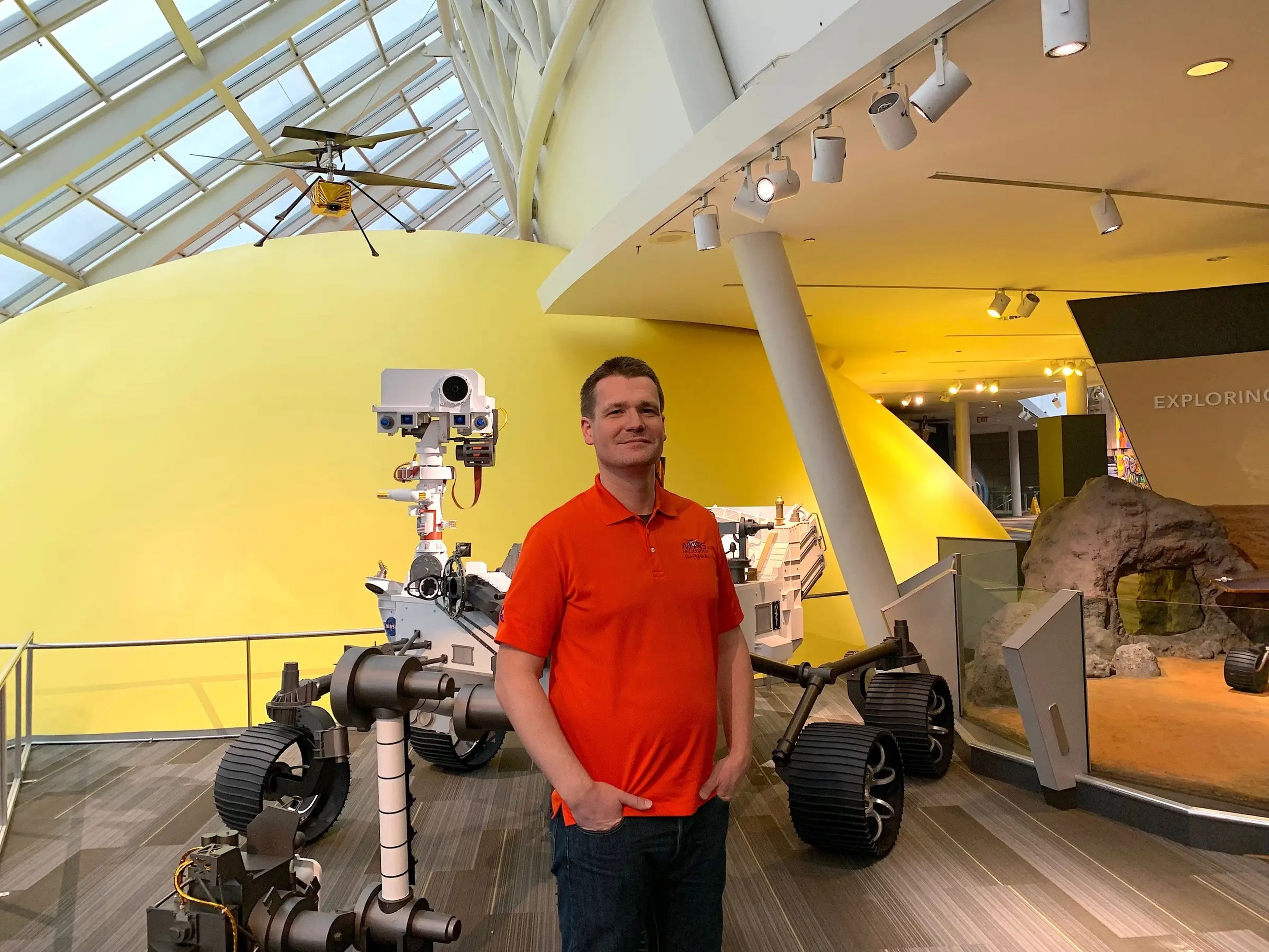 Håvard Grip delante de una maqueta a tamaño real del vehículo explorador Perseverance y del helicóptero Ingenuity (arriba a la izquierda) en el Planetario Adler de Chicago.