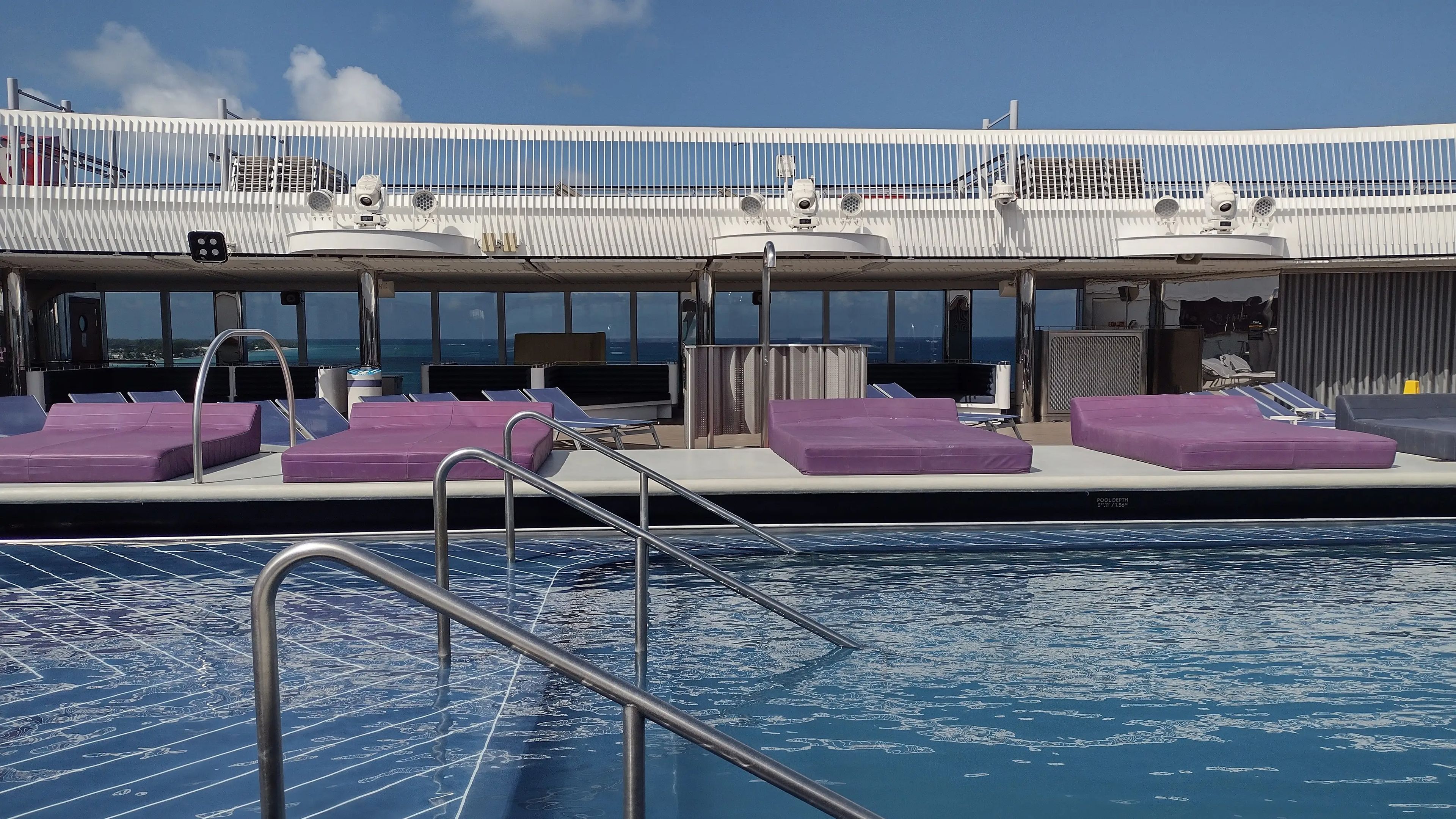A pool on a cruise ship lined with purple daybeds.