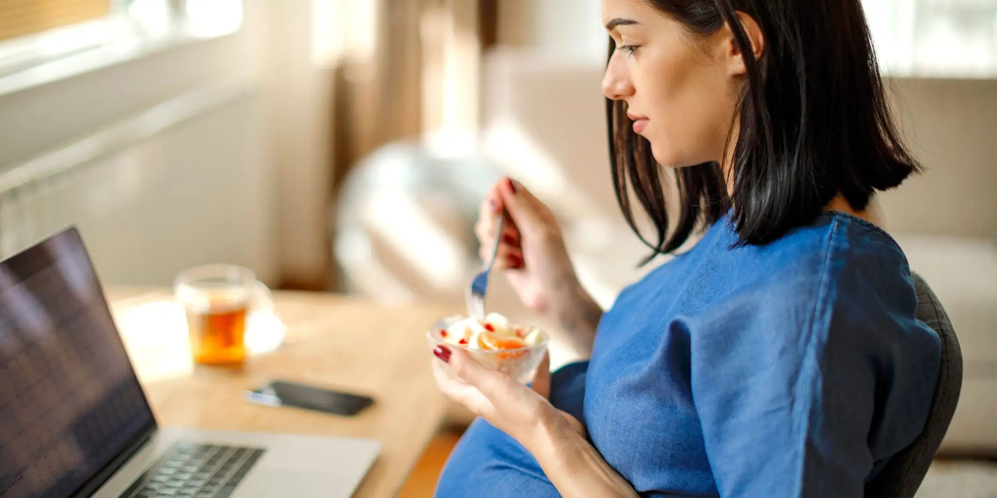 A pregnant woman snacking on a bowl of yogurt and peaches.