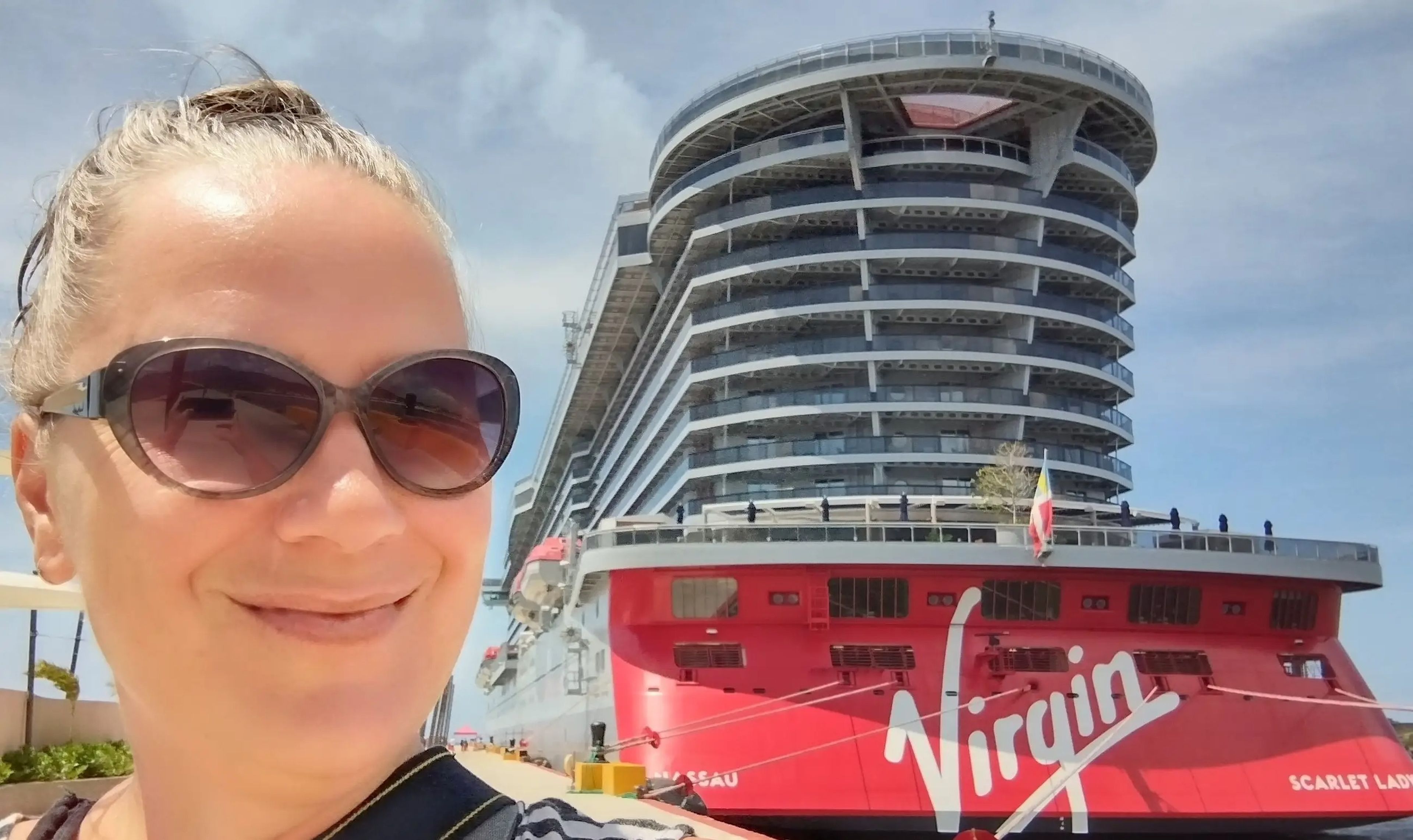 A woman takes a selfie in front of a Virgin cruise ship.