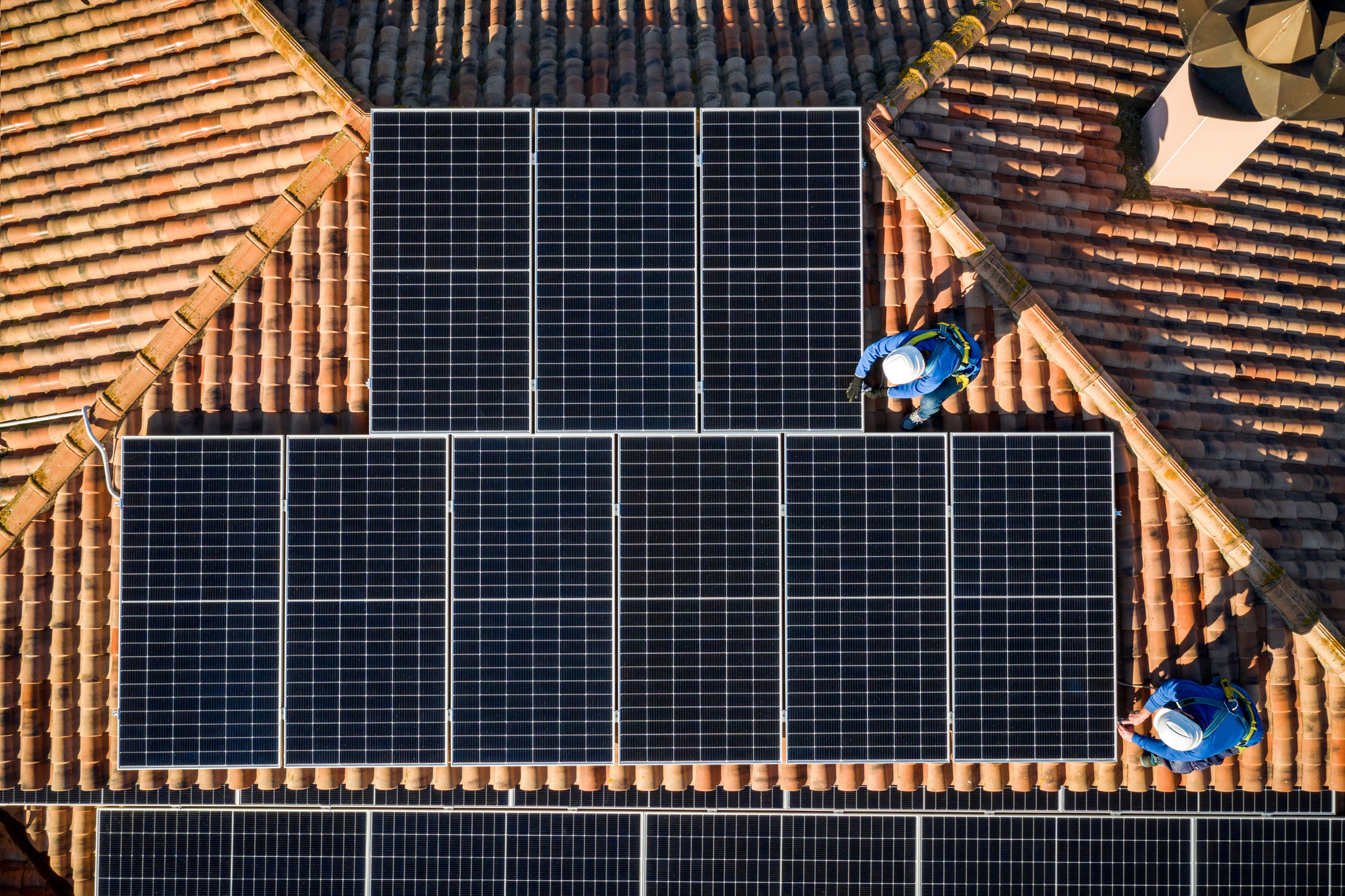 2 personas instalan unas placas solares en un tejado.
