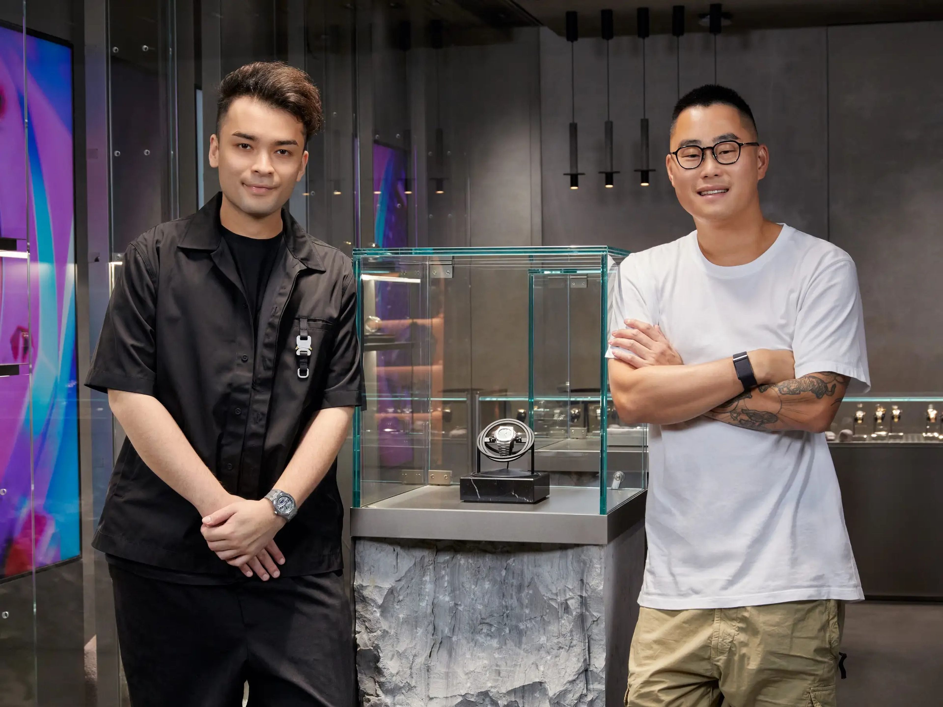 Austen Chu and Sean Wong stand next to a watch in a glass case