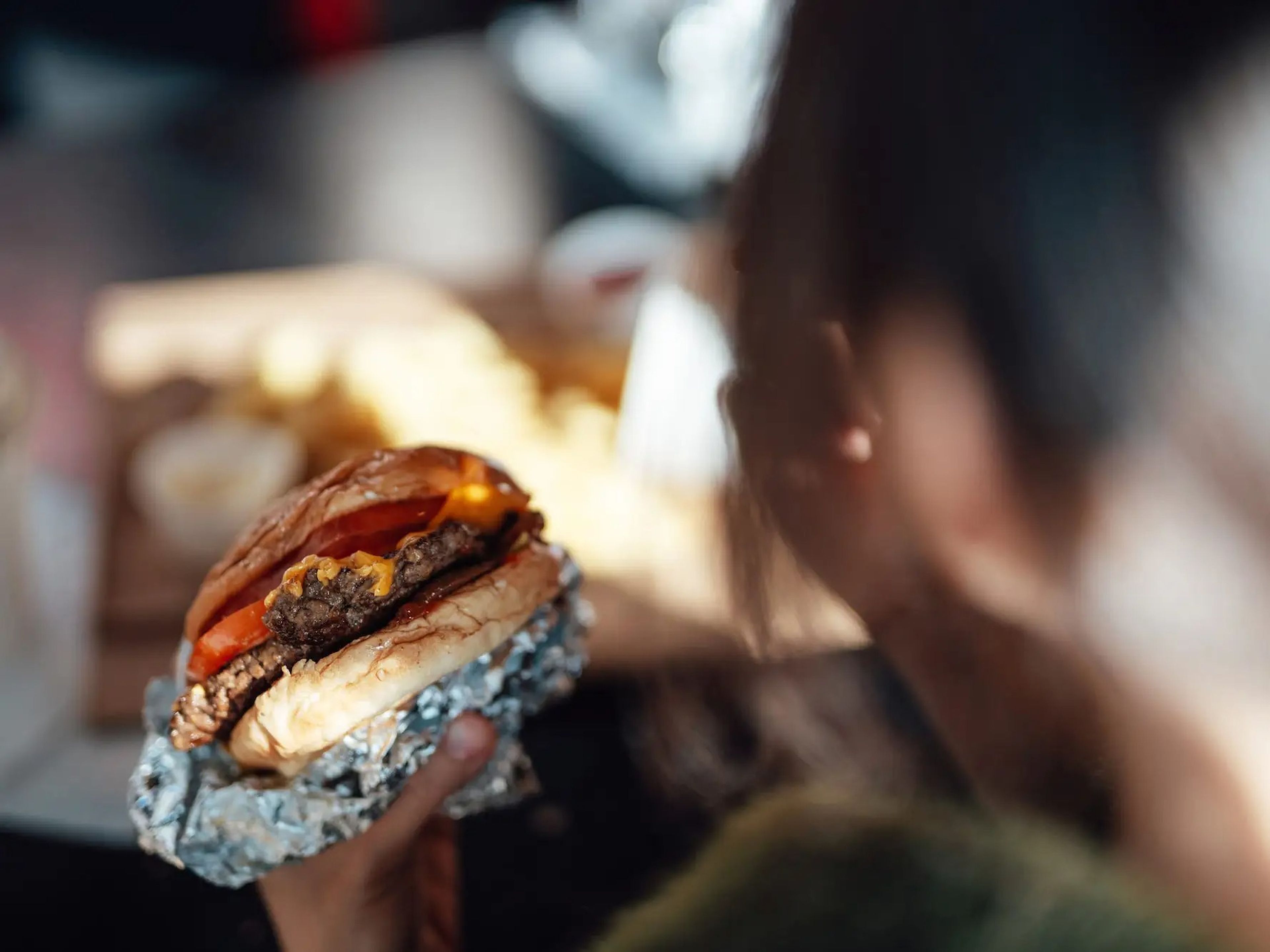 A burger is seen being held up ready to be eaten over a person's shoulder.