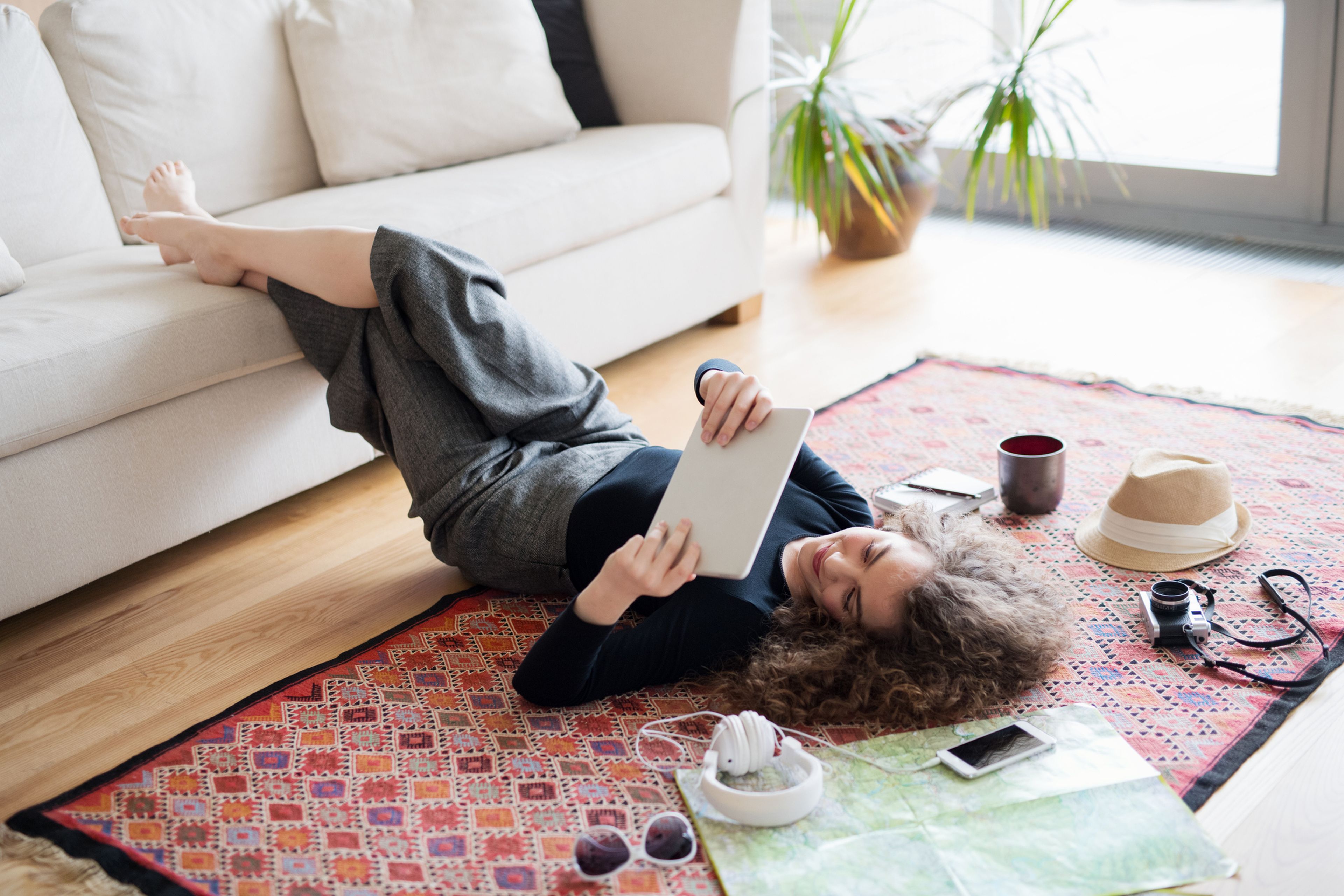 Chica joven con una tablet, tumbada sobre el sofá, en casa