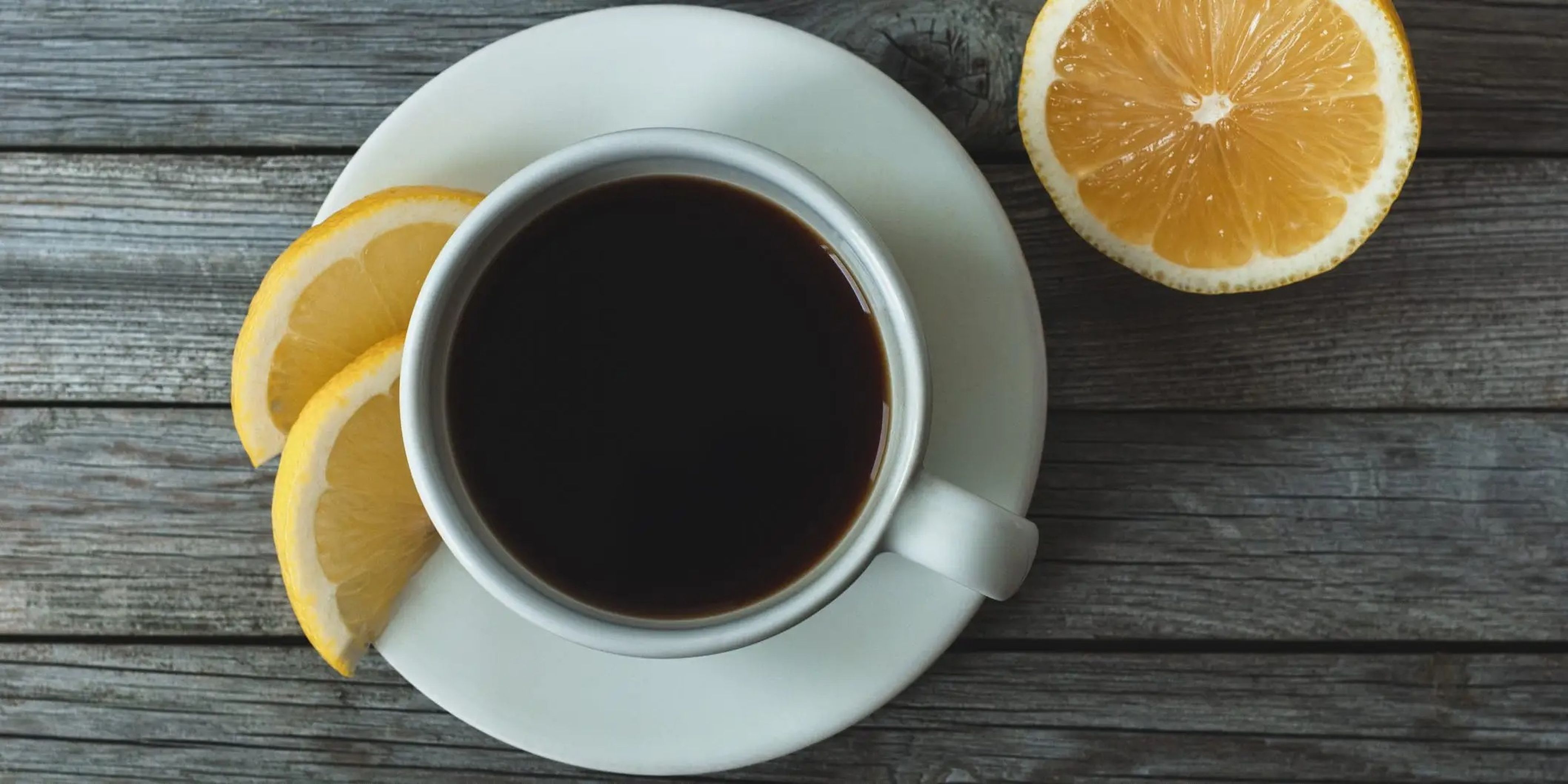 A cup of coffee set on a plate with slices of lemon surrounding it.