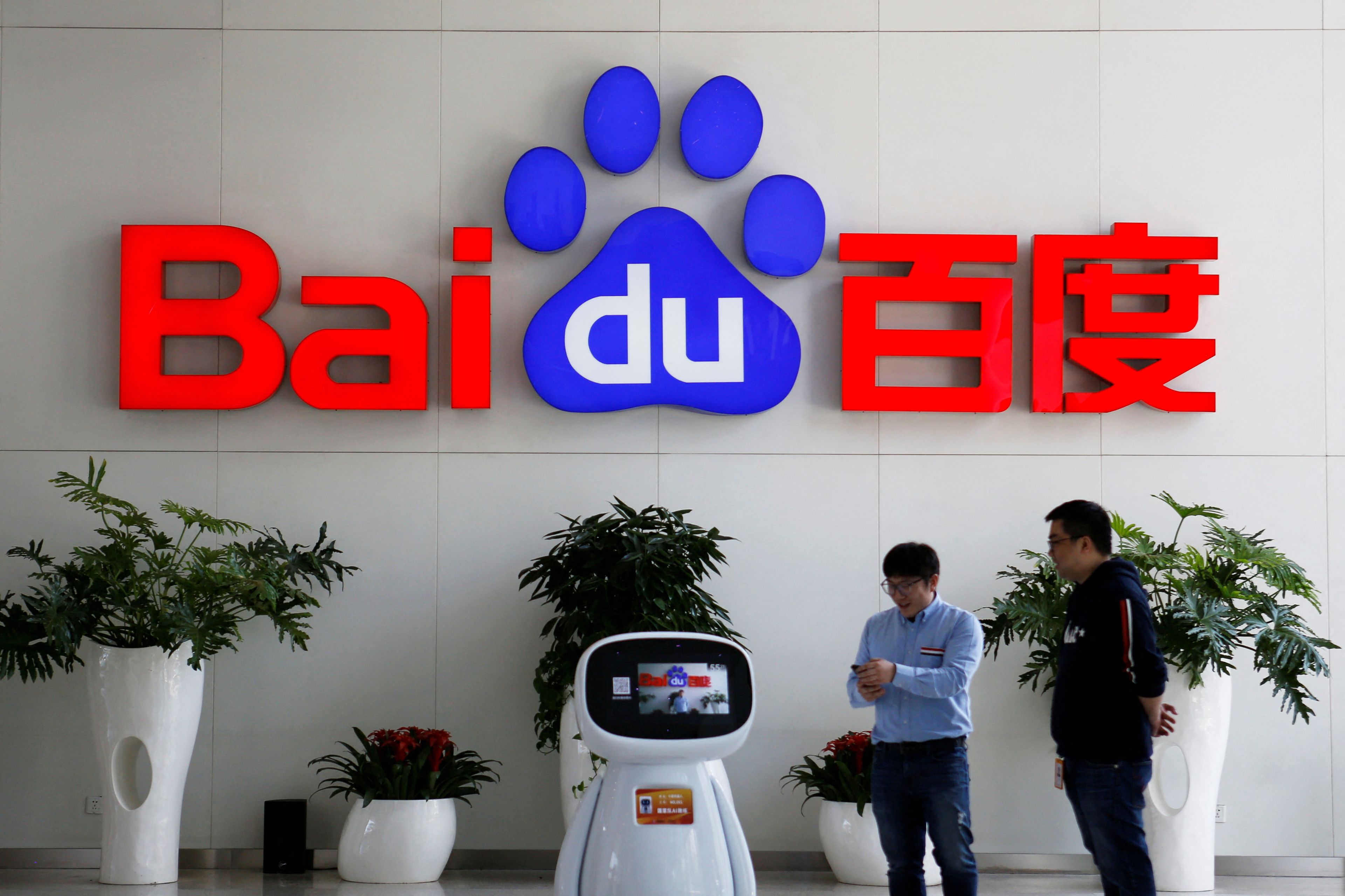 Dos personas interactúan con un robot de Baidu cerca del logotipo de la empresa en su sede de Pekín (China).