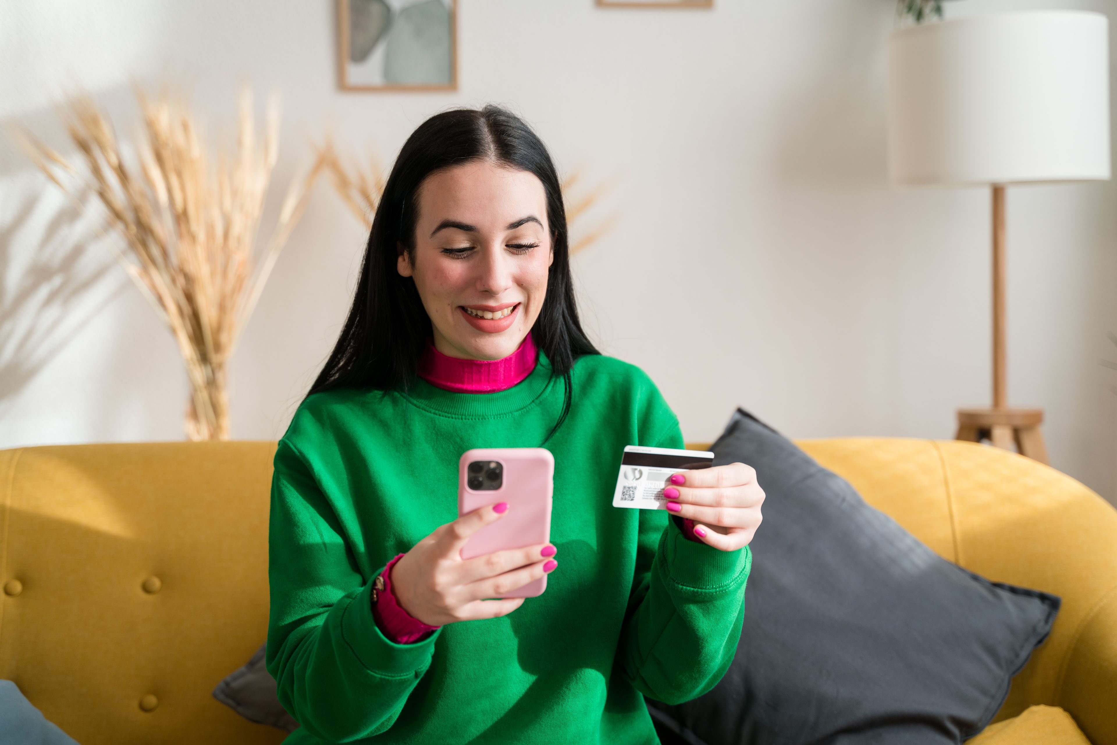 Mujer joven mira el móvil y la tarjeta bancaria