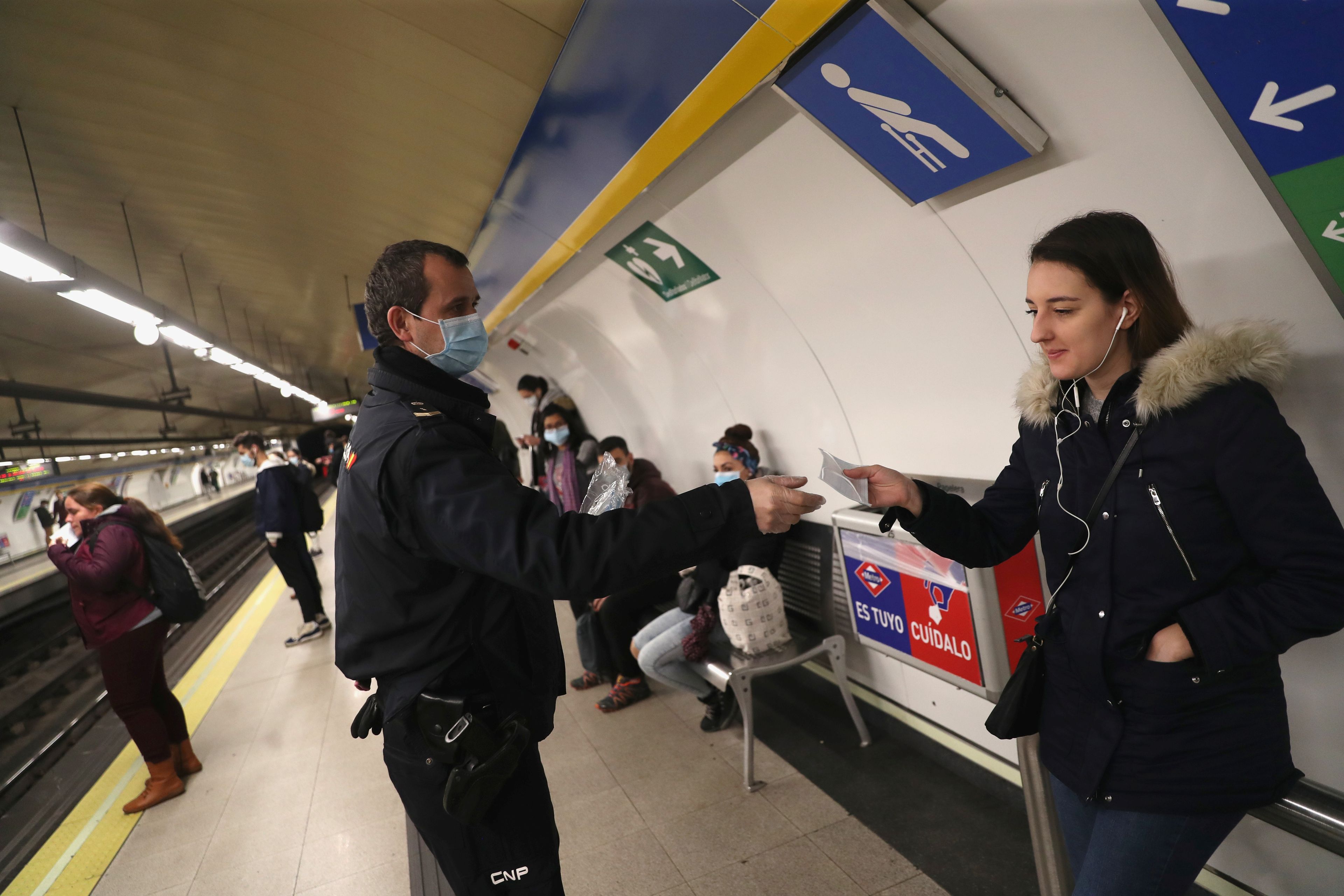 Un policía entrega una mascarilla a una mujer, en el metro de Madrid