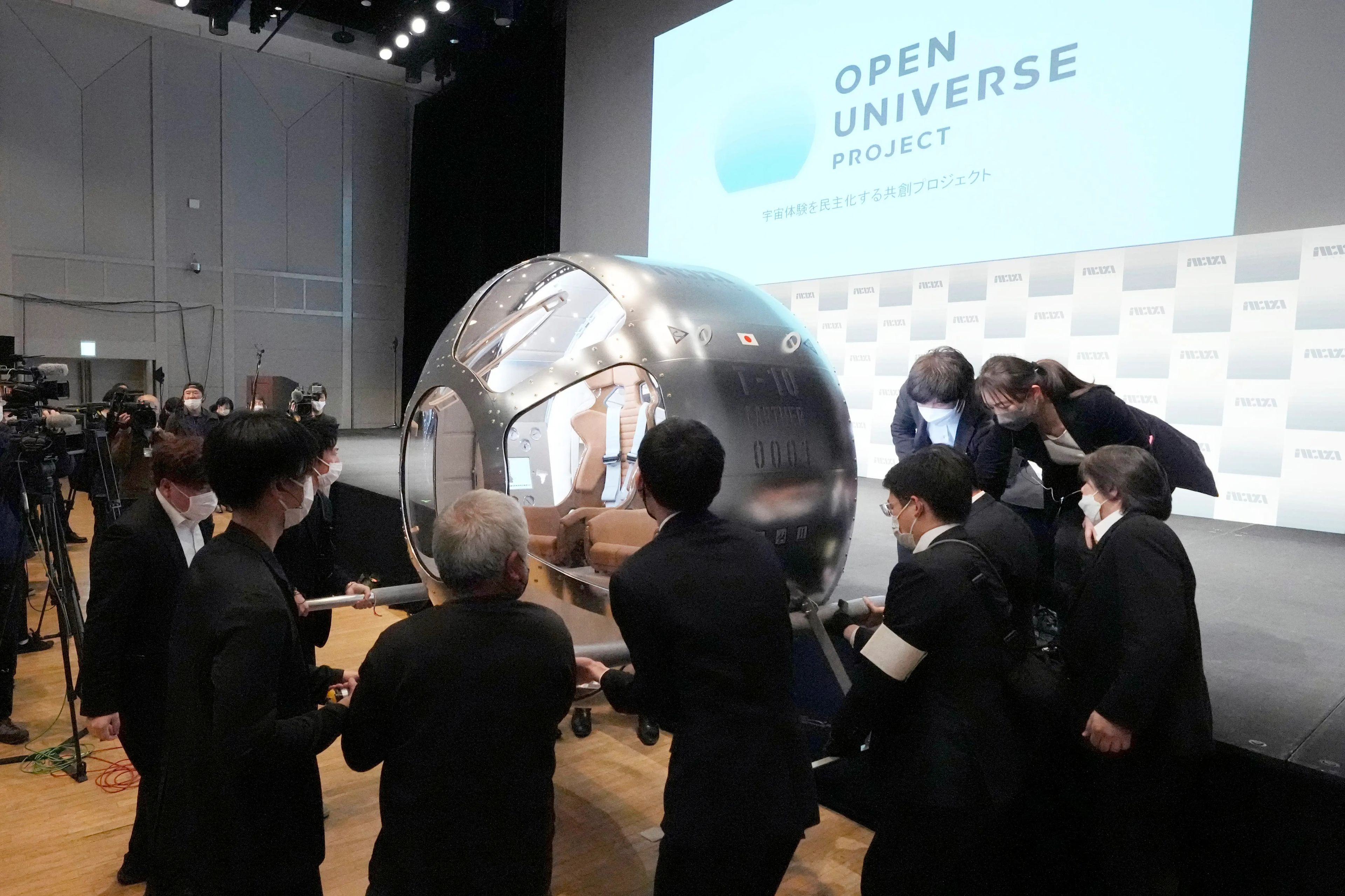 Empleados de una empresa emergente japonesa llevan un prototipo de su nave espacial al escenario durante una rueda de prensa.
