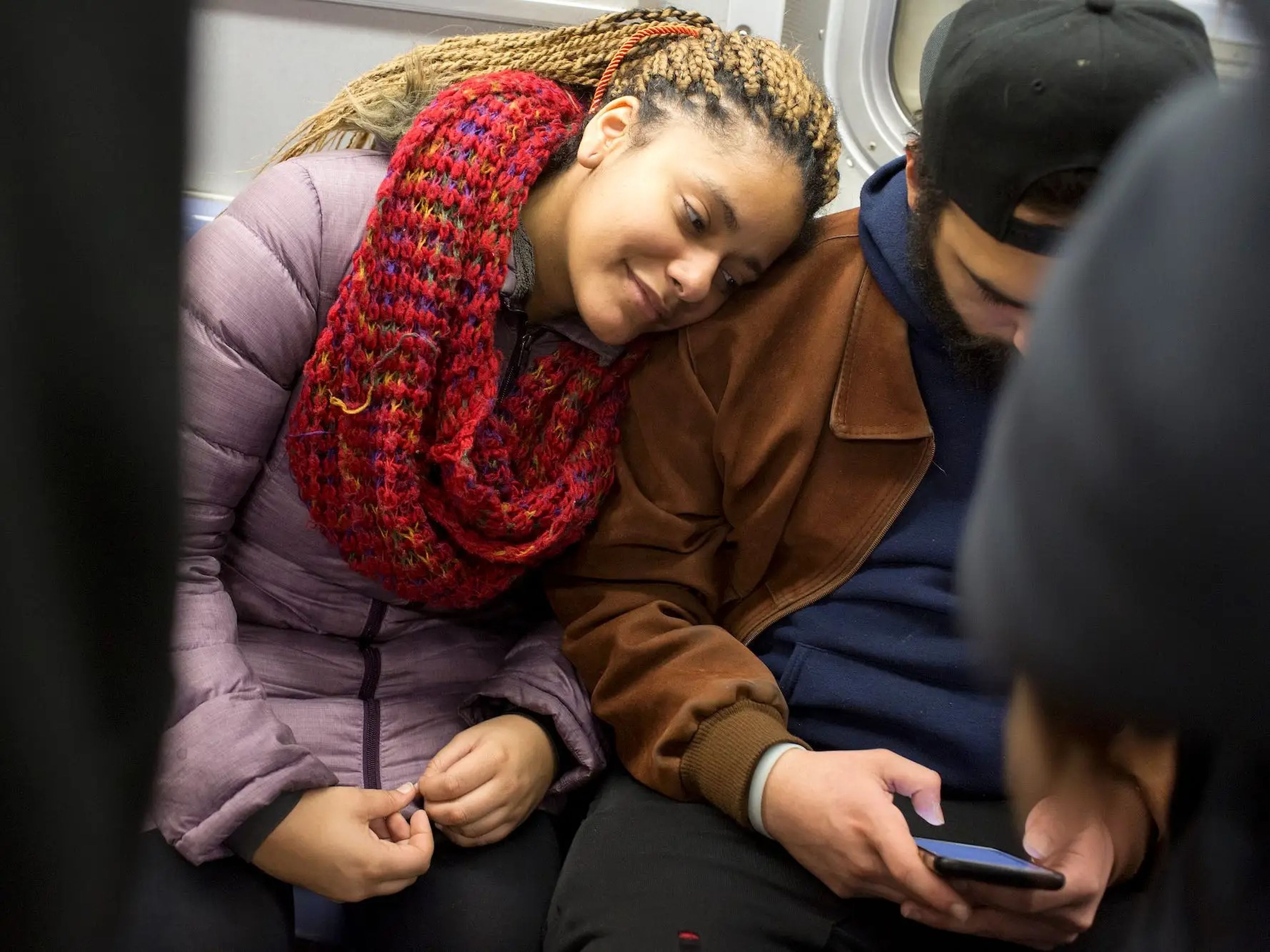 A woman smiles as she leans on her partner's shoulder, looking at a phone he is holding.