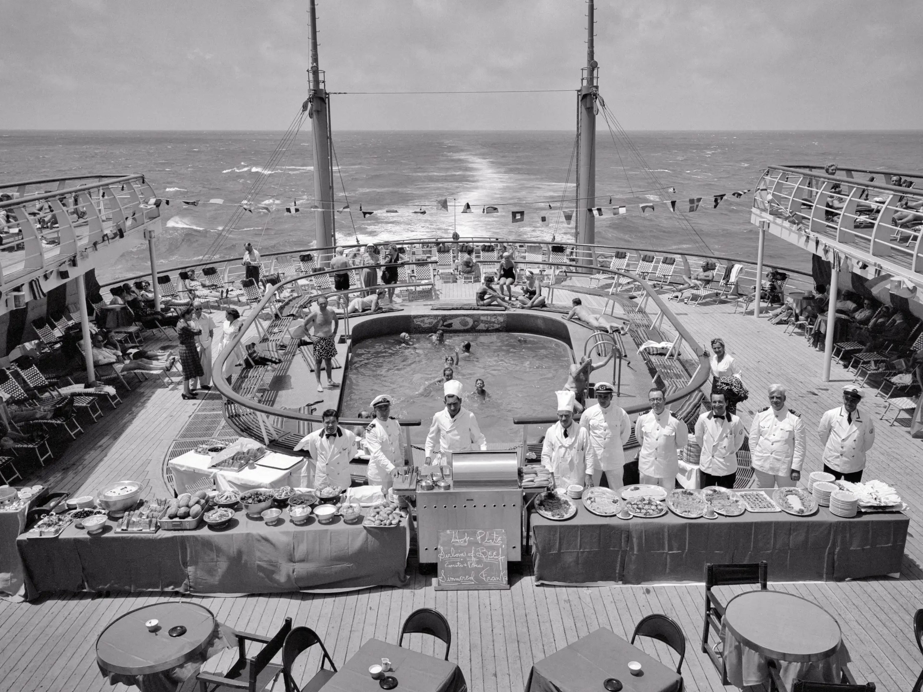 1950s Buffet Lunch Serving Crew Staff Assembled Aboard The Aft Deck By Swimming Pool On The Cruise Ship Independence At Sea.