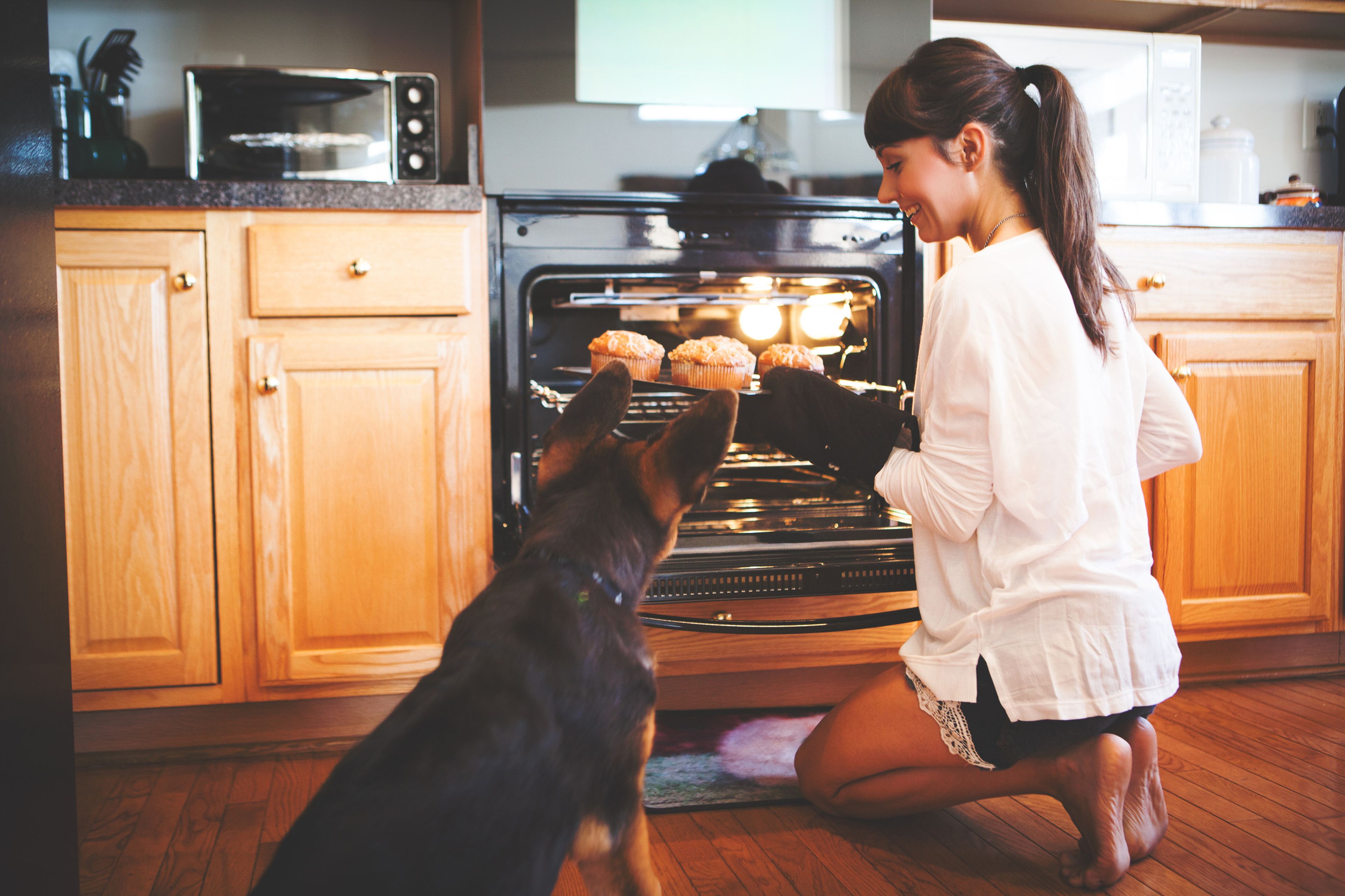 Una chica saca unas magdalenas del horno ante la mirada de su perro.