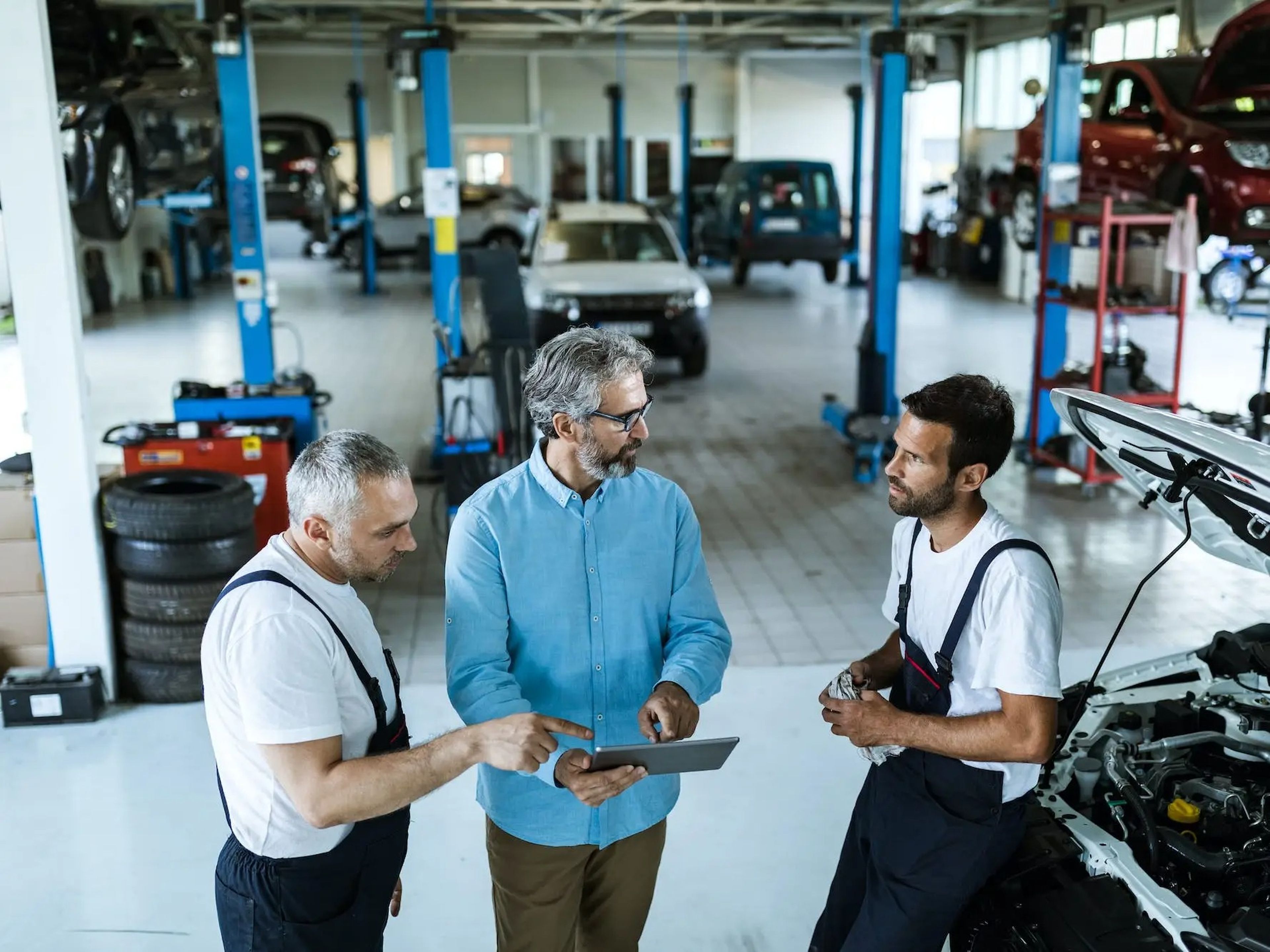 Gerente utilizando una tablet mientras habla con los mecánicos en un taller de reparación de automóviles.