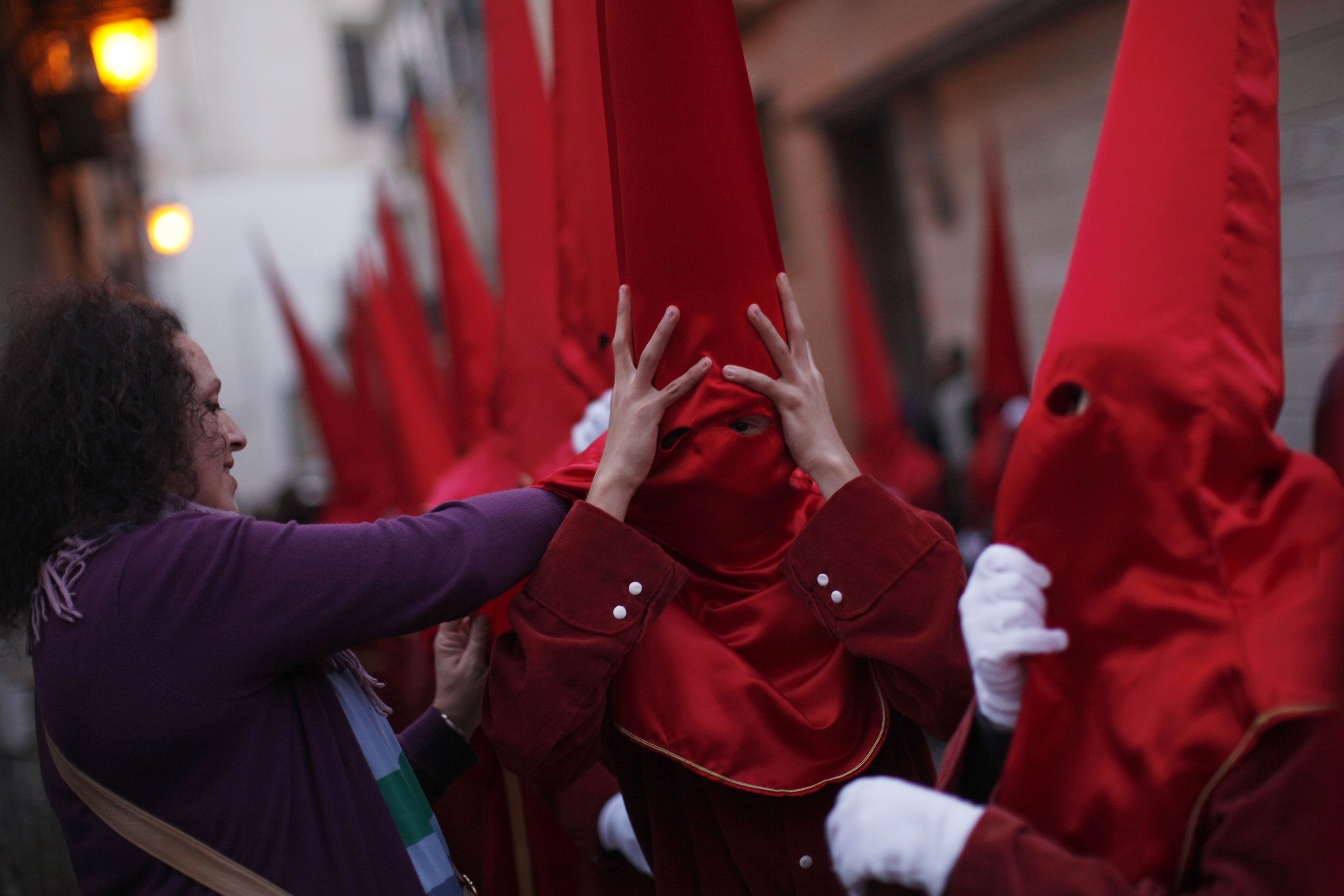 Una mujer ajusta el capirote a un nazareno de la cofradía de La Sangre en la Semana Santa de Málaga.