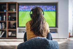 Una mujer jugando a un videojuego de fútbol con auriculares.