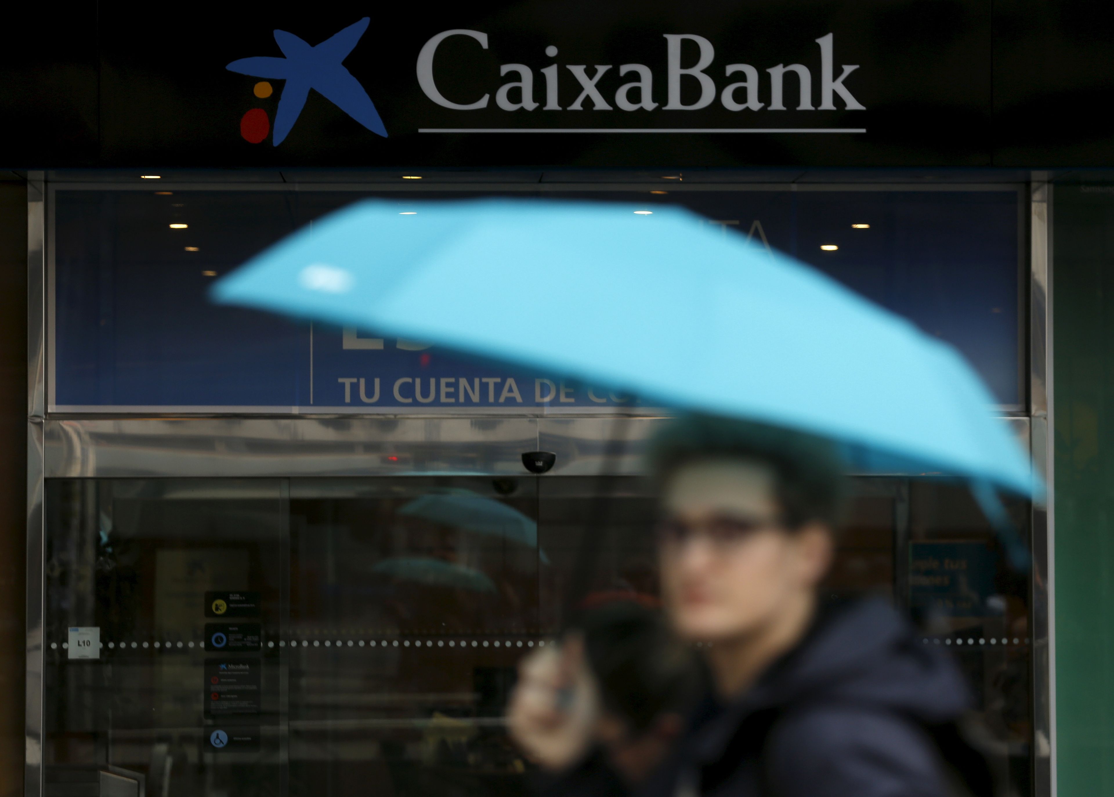 Una persona pasando con un paraguas frente al banco CaixaBank