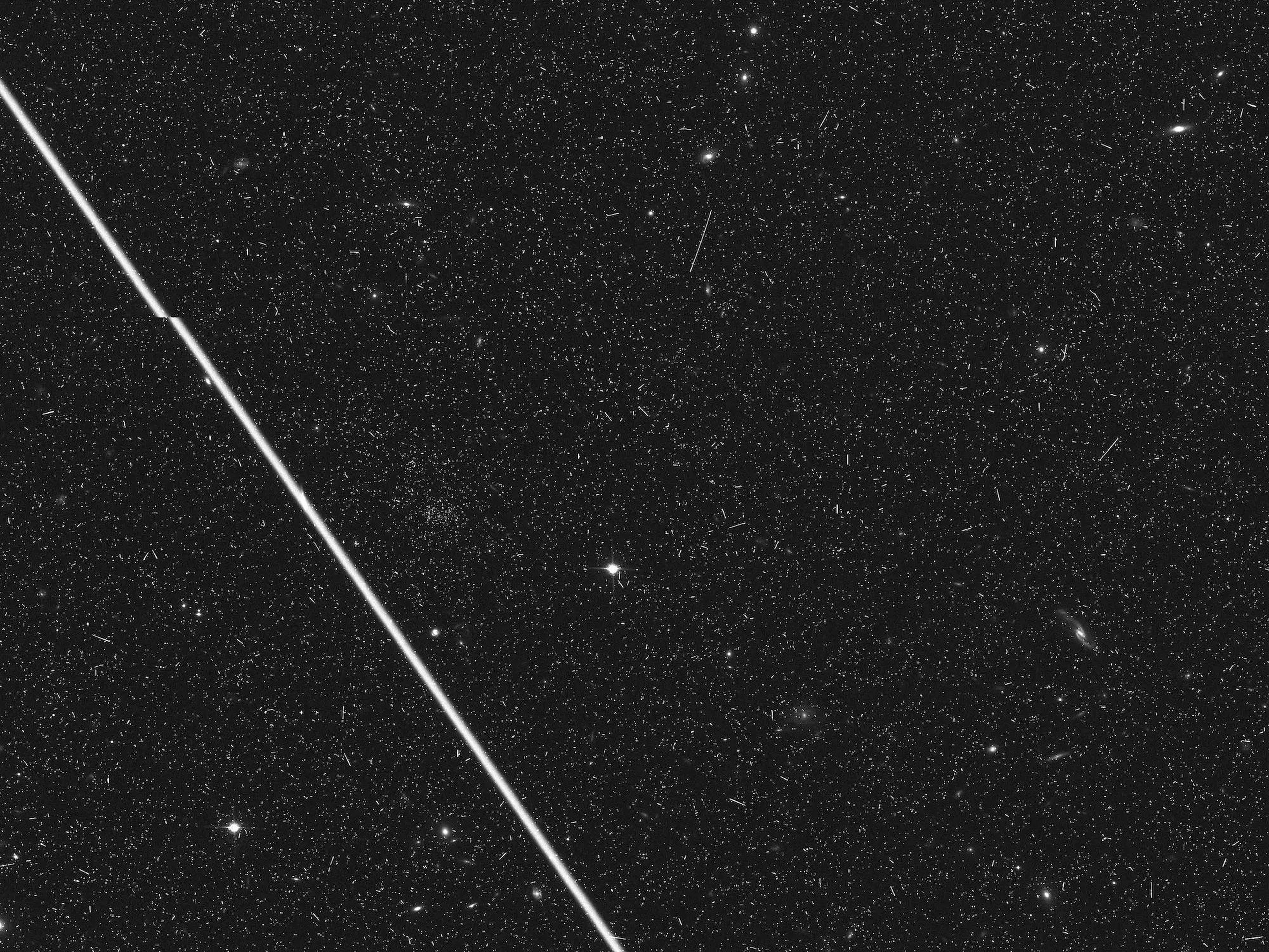 Un satélite traza una gruesa línea blanca en una fotografía del Hubble.