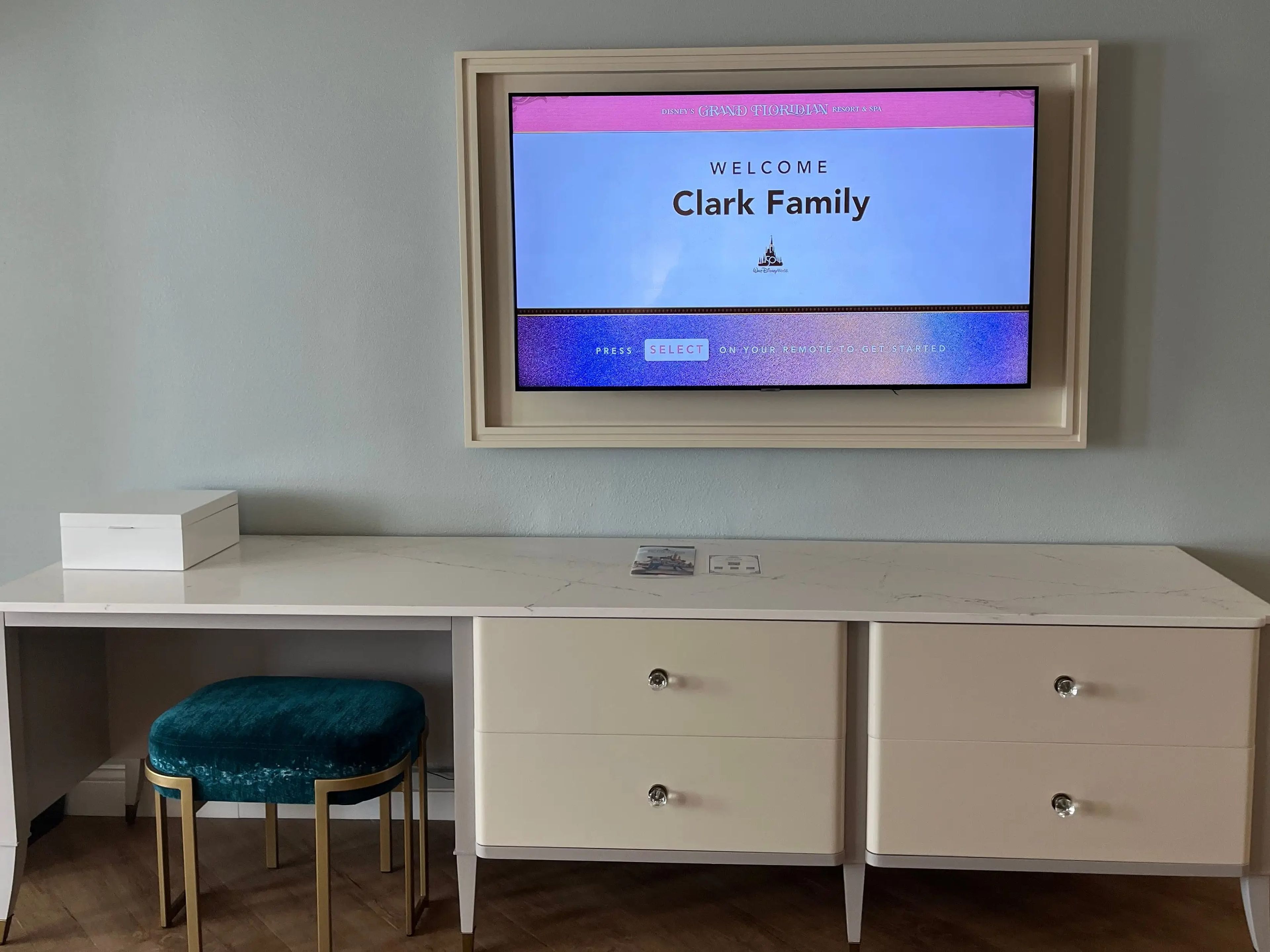 tv over a desk with drawers in a grand floridian resort room with a screen that reads "clark family"