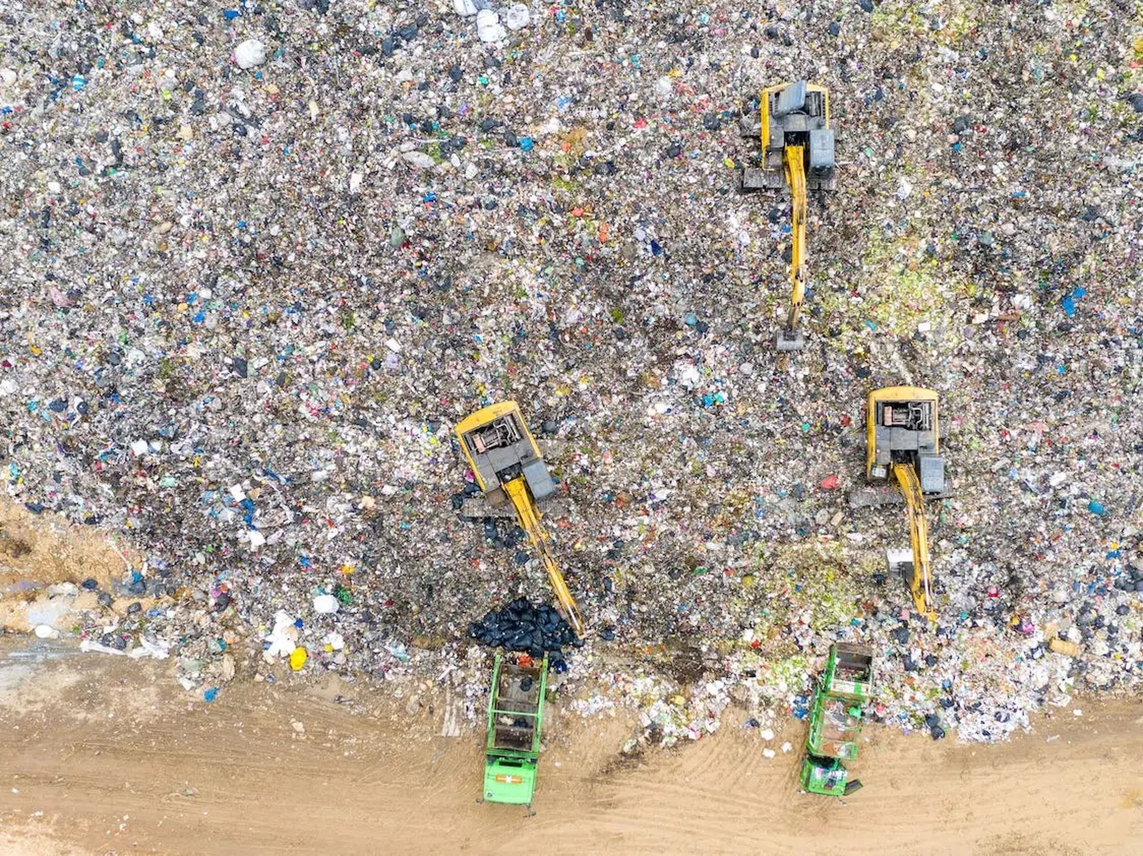 Aerial shot of garbage trucks unloading trash into a landfill.