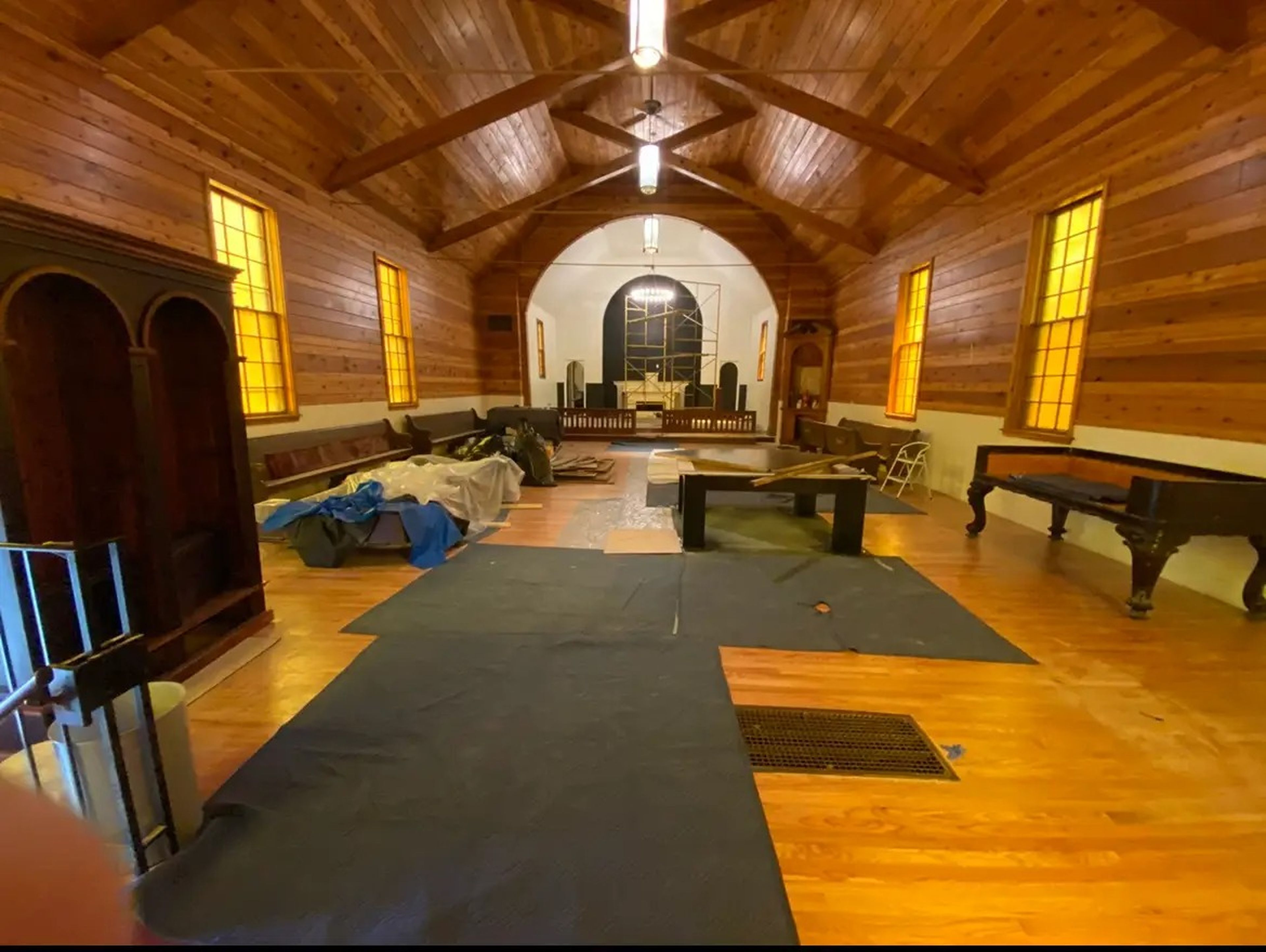 A church nave with wood walls and moving blankets on the floors.