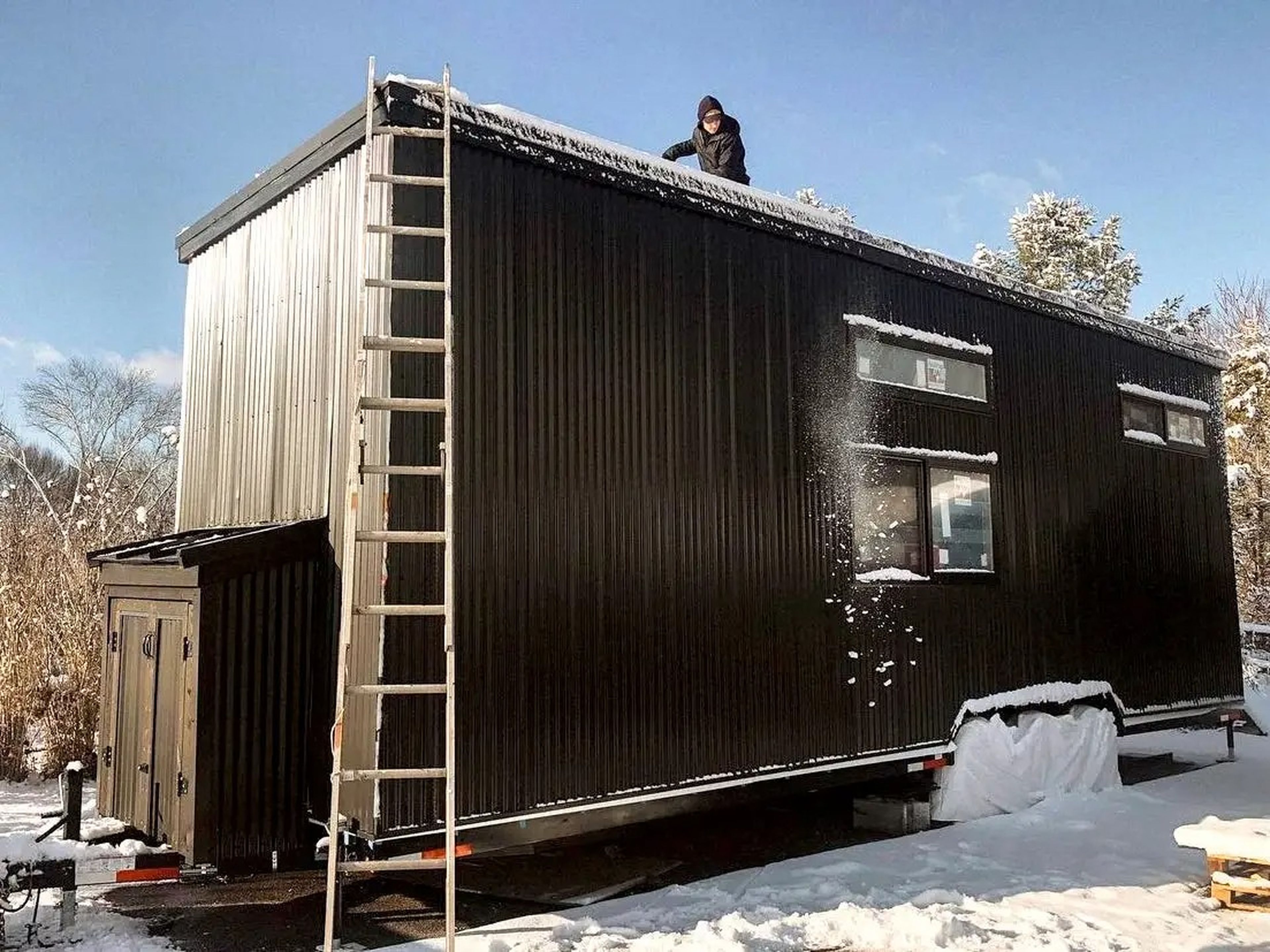 Exterior of black tiny house surrounded by snow and trees