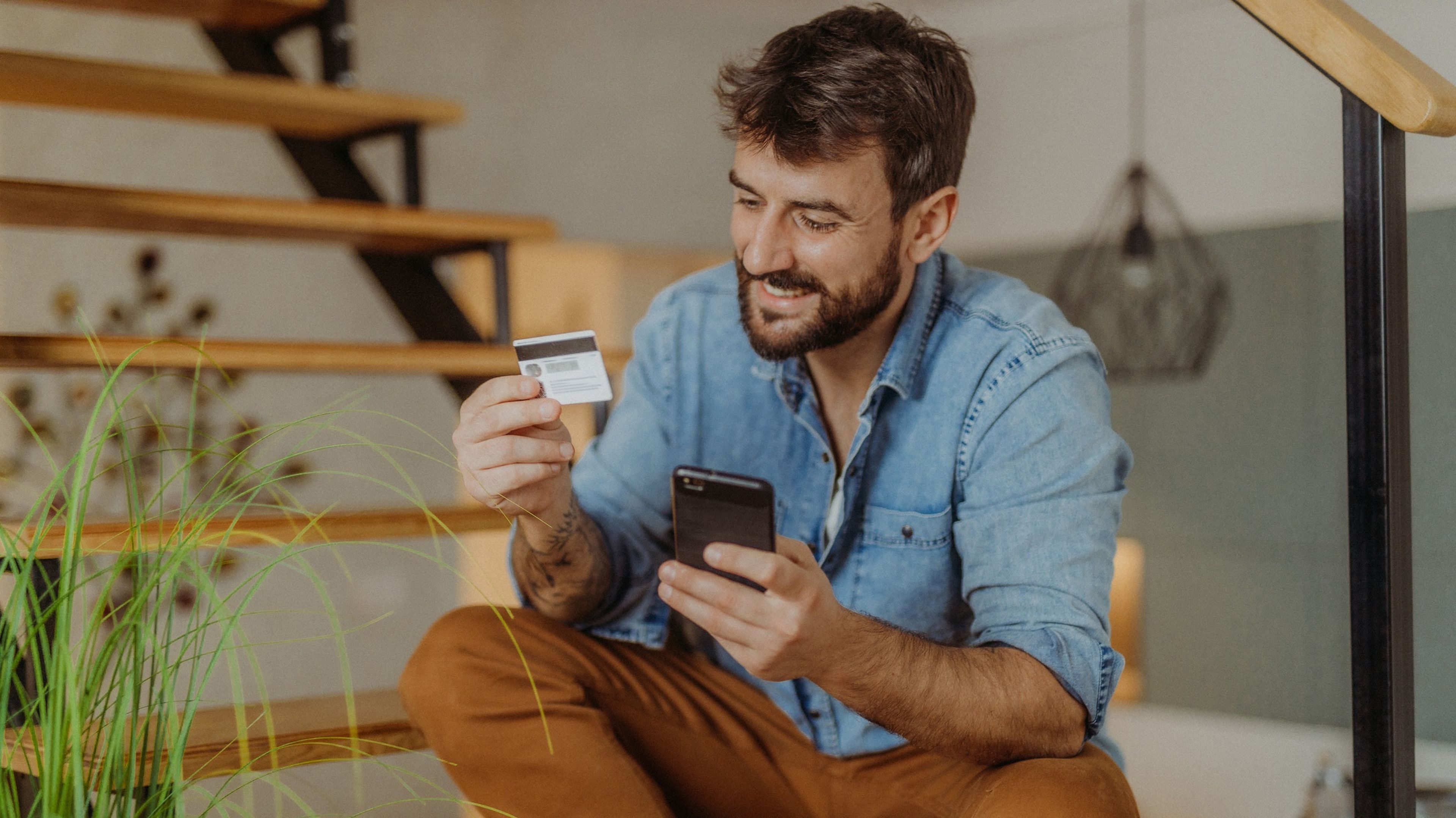Hombre realizando una compra con un móvil y una tarjeta de crédito en la mano