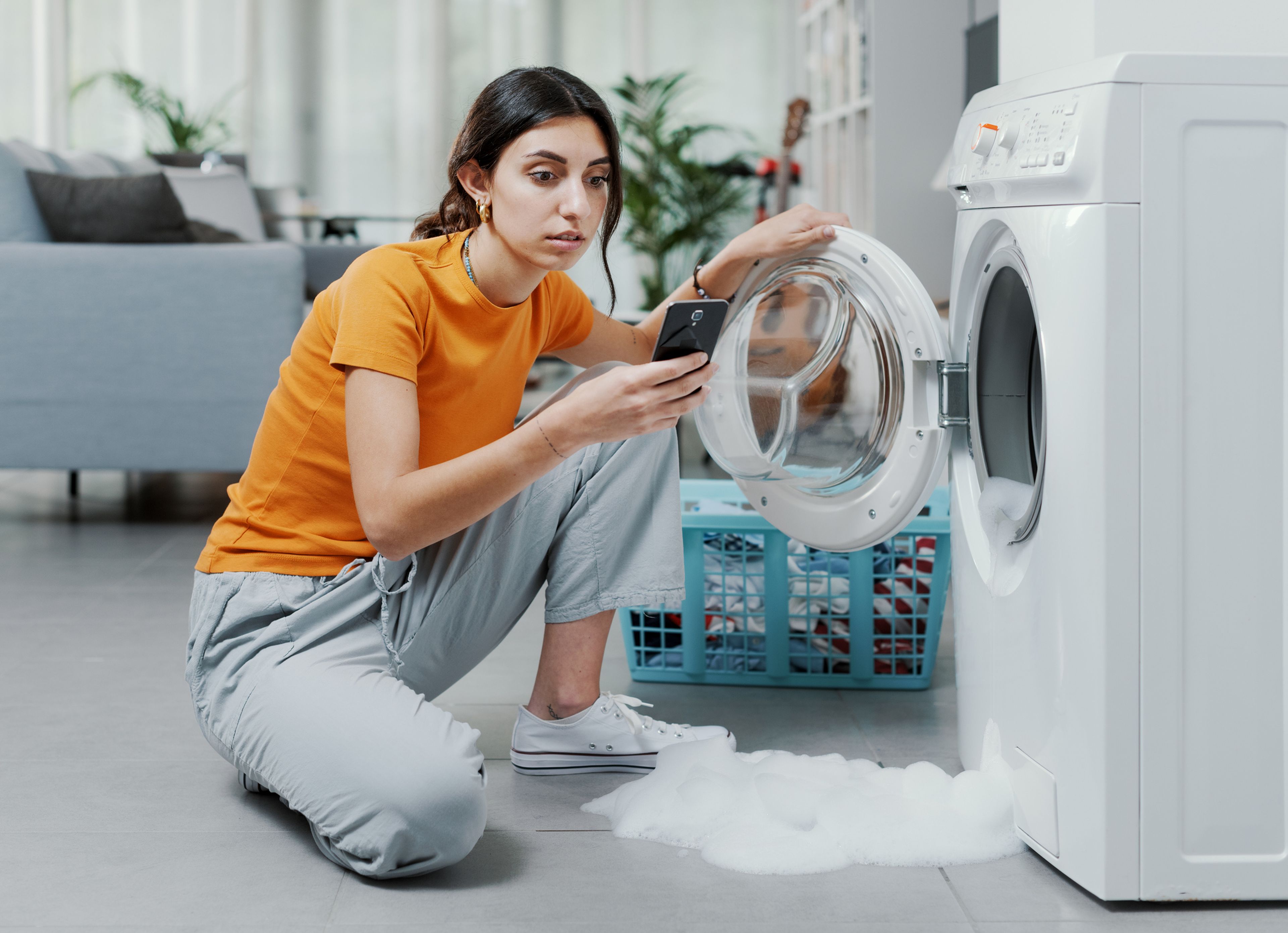 Una mujer mira el móvil con la lavadora rota.
