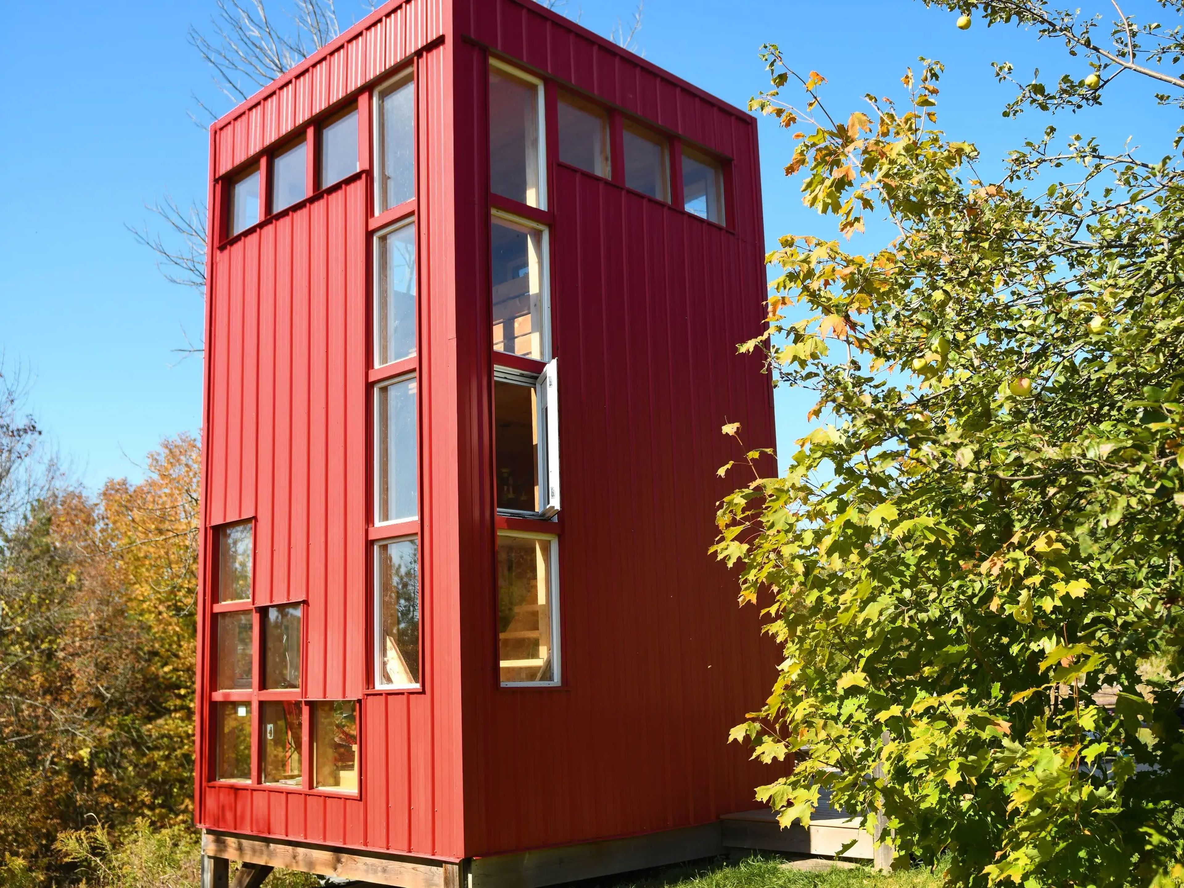 Photo of the red tower tiny house rental from a distance. It has several square windows.