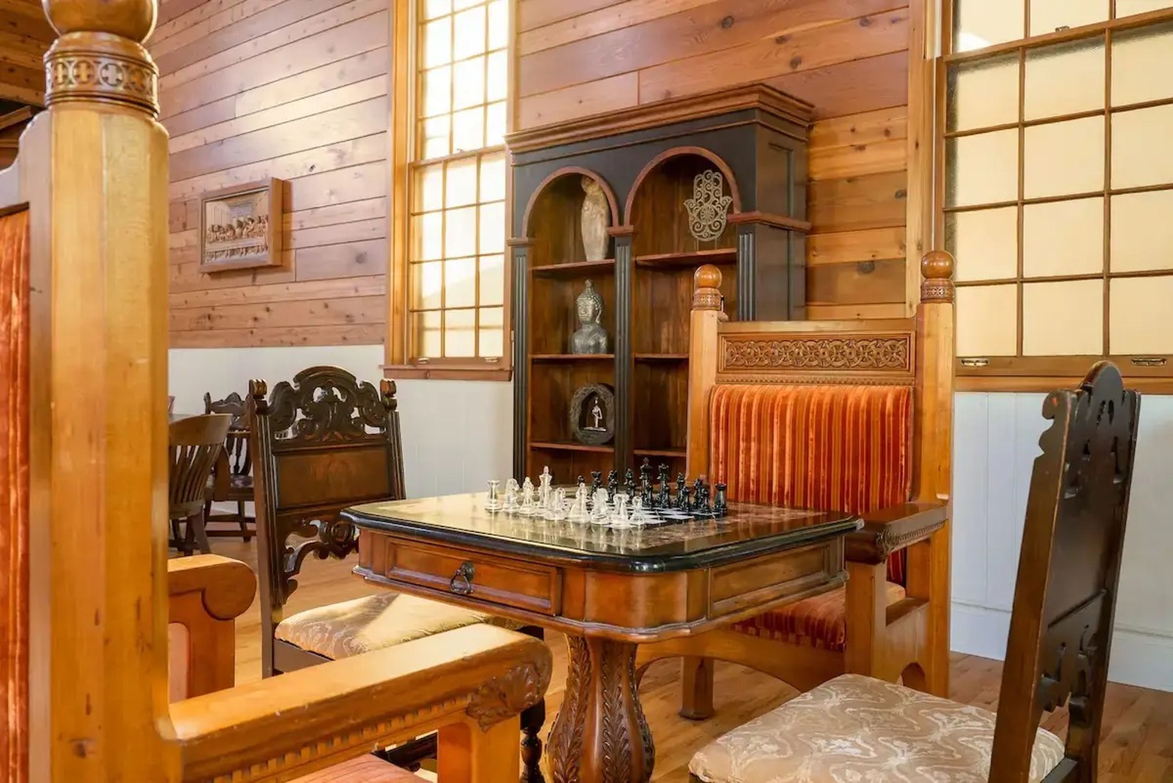 A room with wood walls and a chess table surrounded by intricate wood chairs.