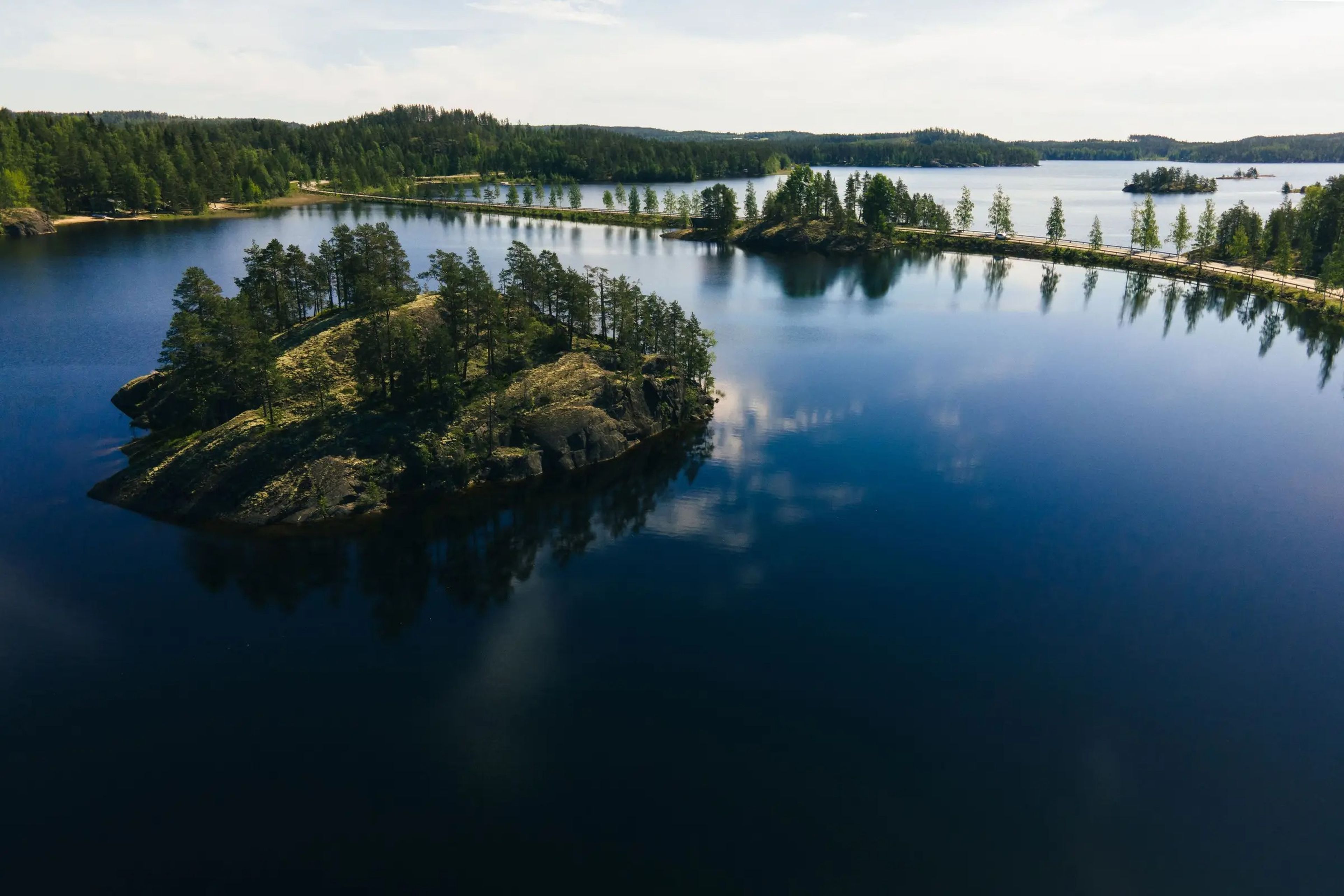 An aerial view across the reflective surface of Lake Saimaa in Puumala, Finland, which is ringed by trees.