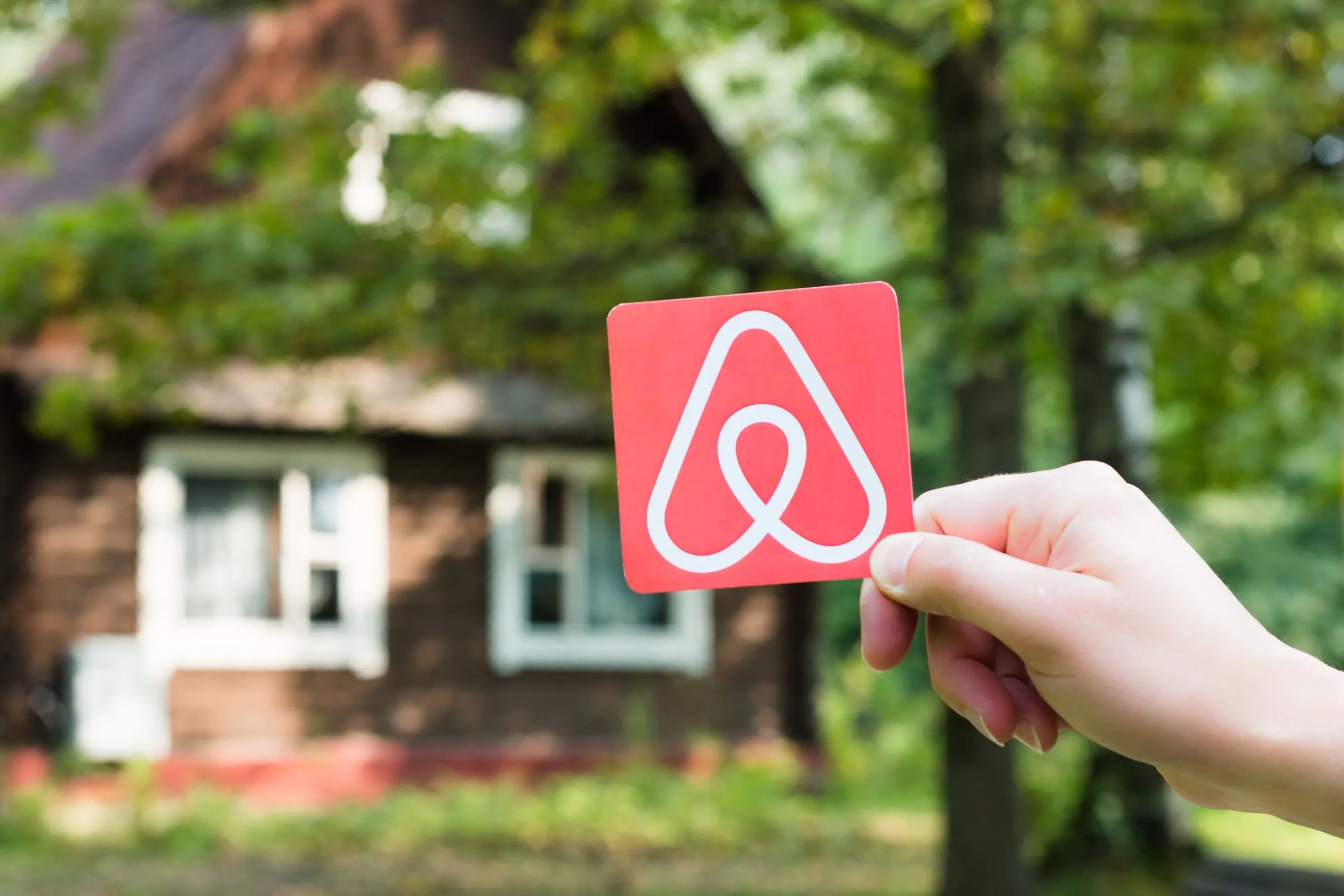 An Airbnb logo held up in front of a rental property.