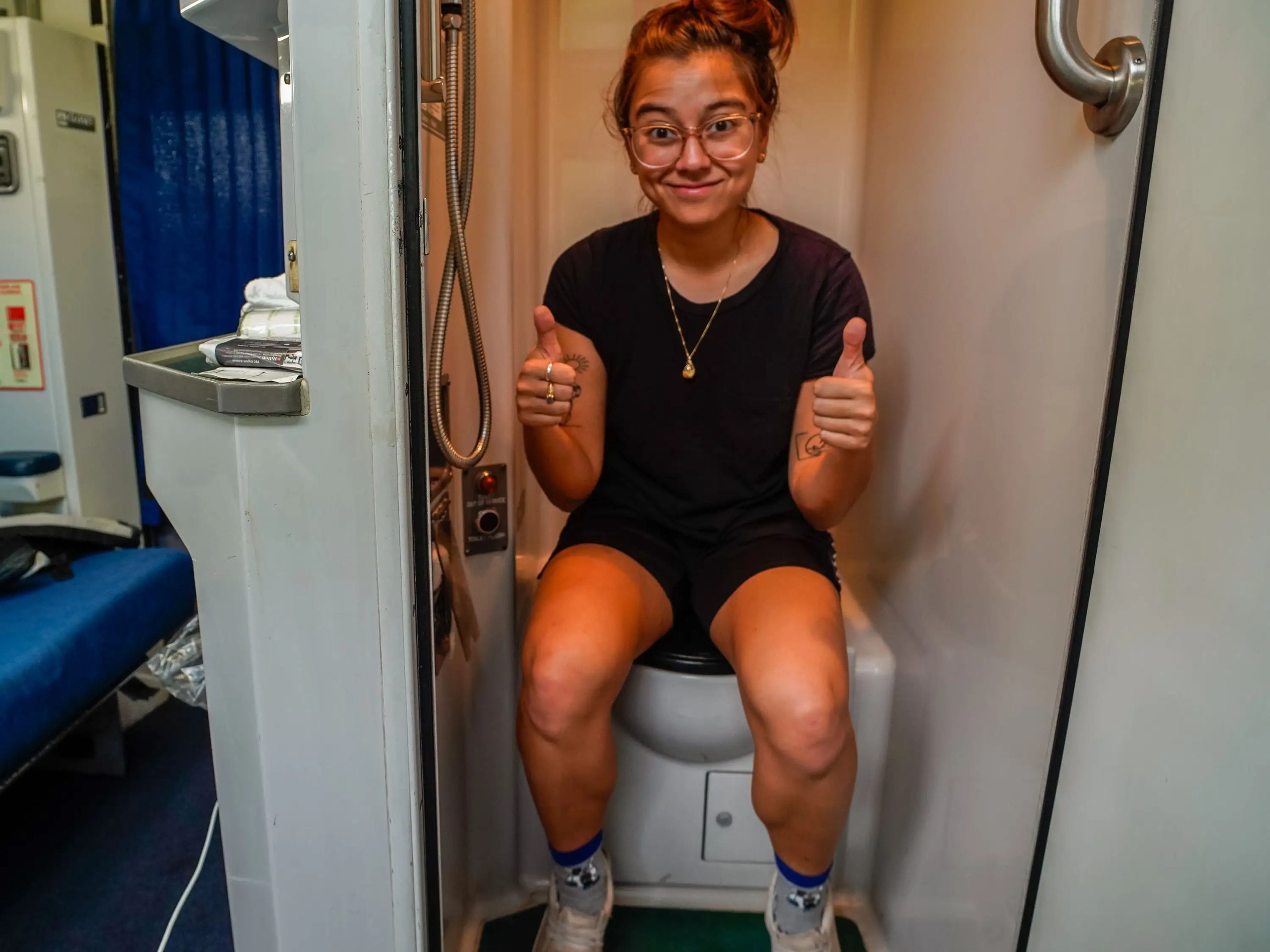 The author sits on the train toilet with her thumbs up