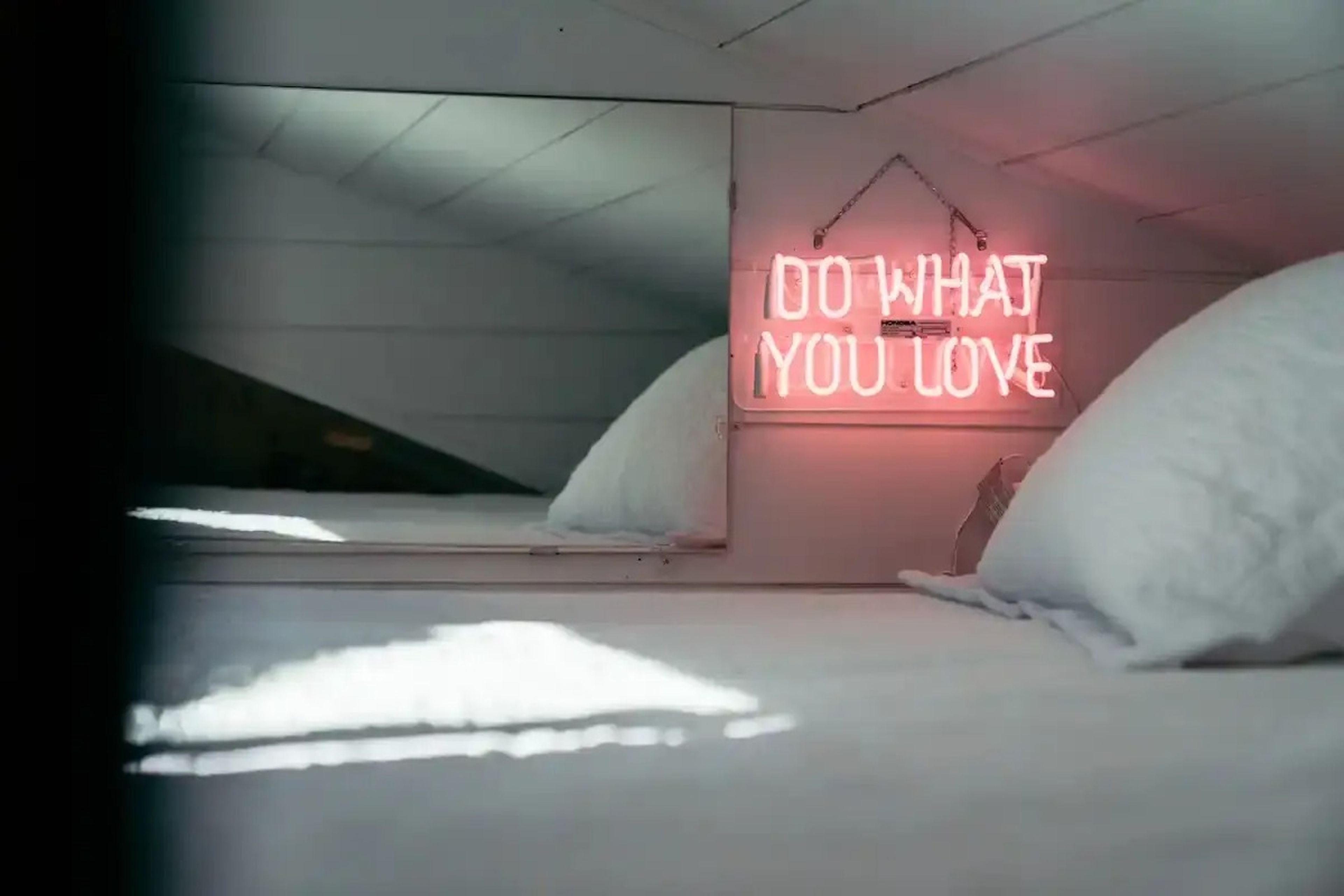 A bed in Ansel Troy's Airbnb with a pink neon sign that reads "Do what you love".