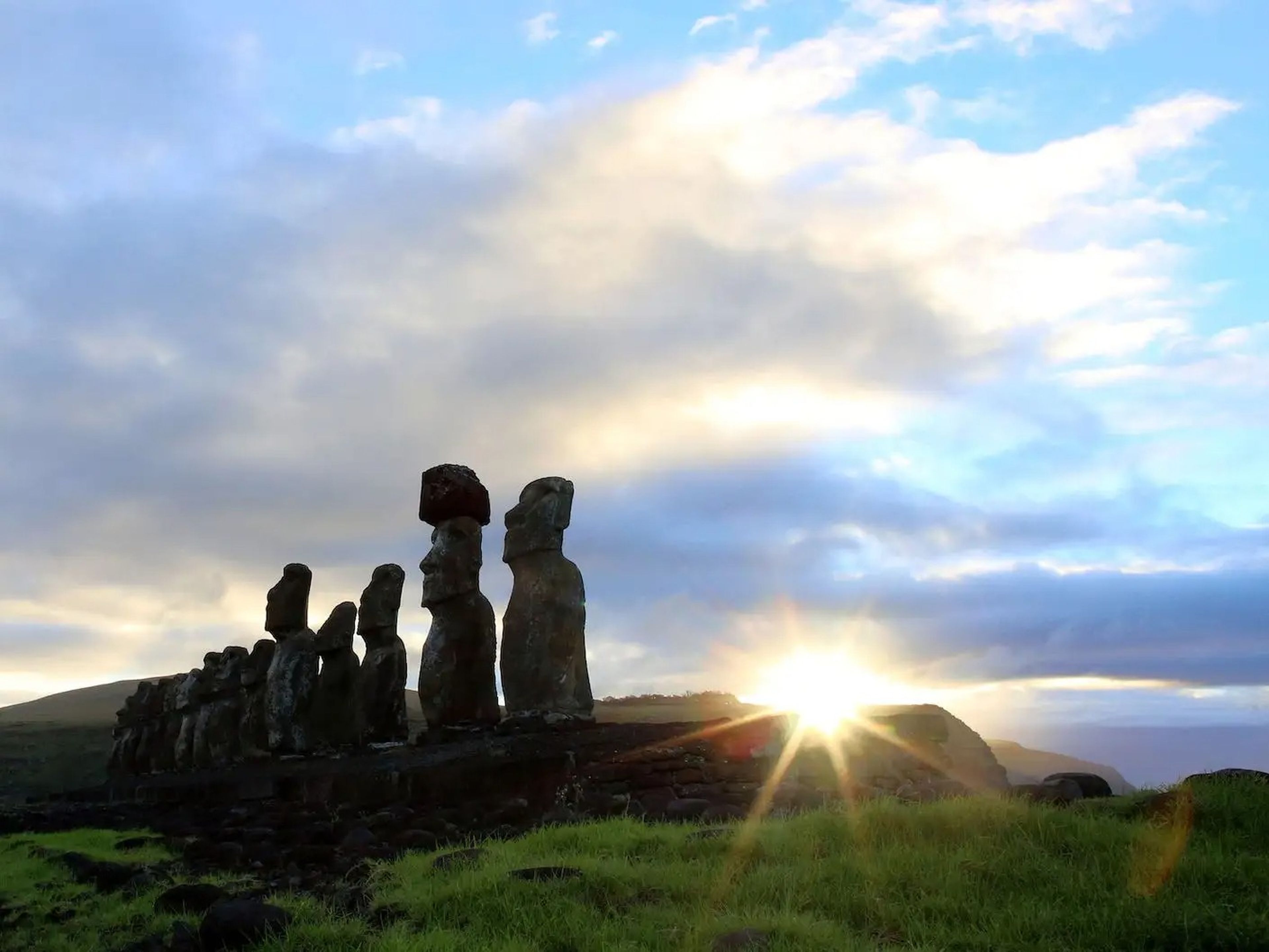 Easter Island heads on a hill with the sun breaking over the horizon.