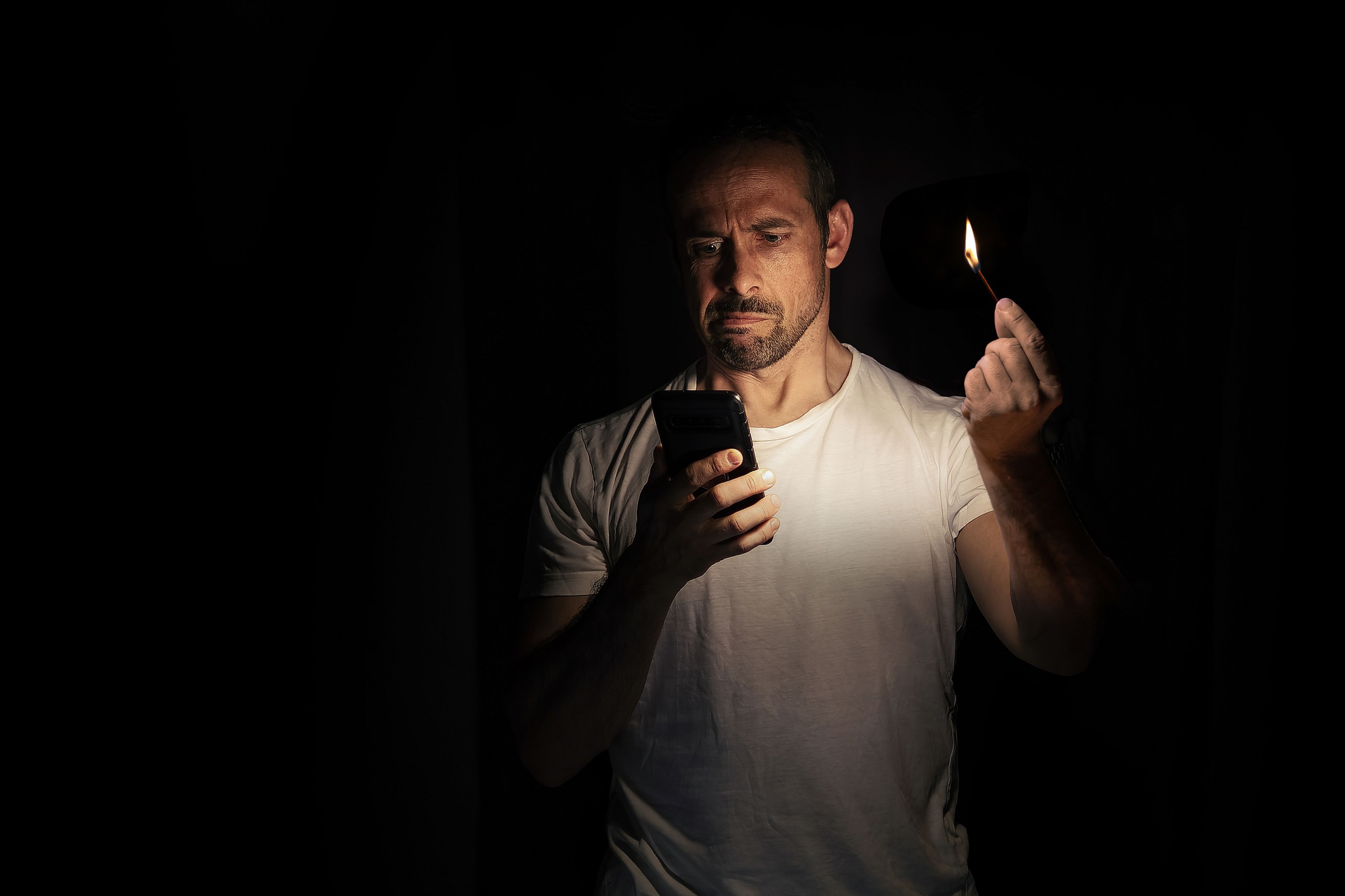 Un hombre mira el móvil, iluminándose con una cerilla.