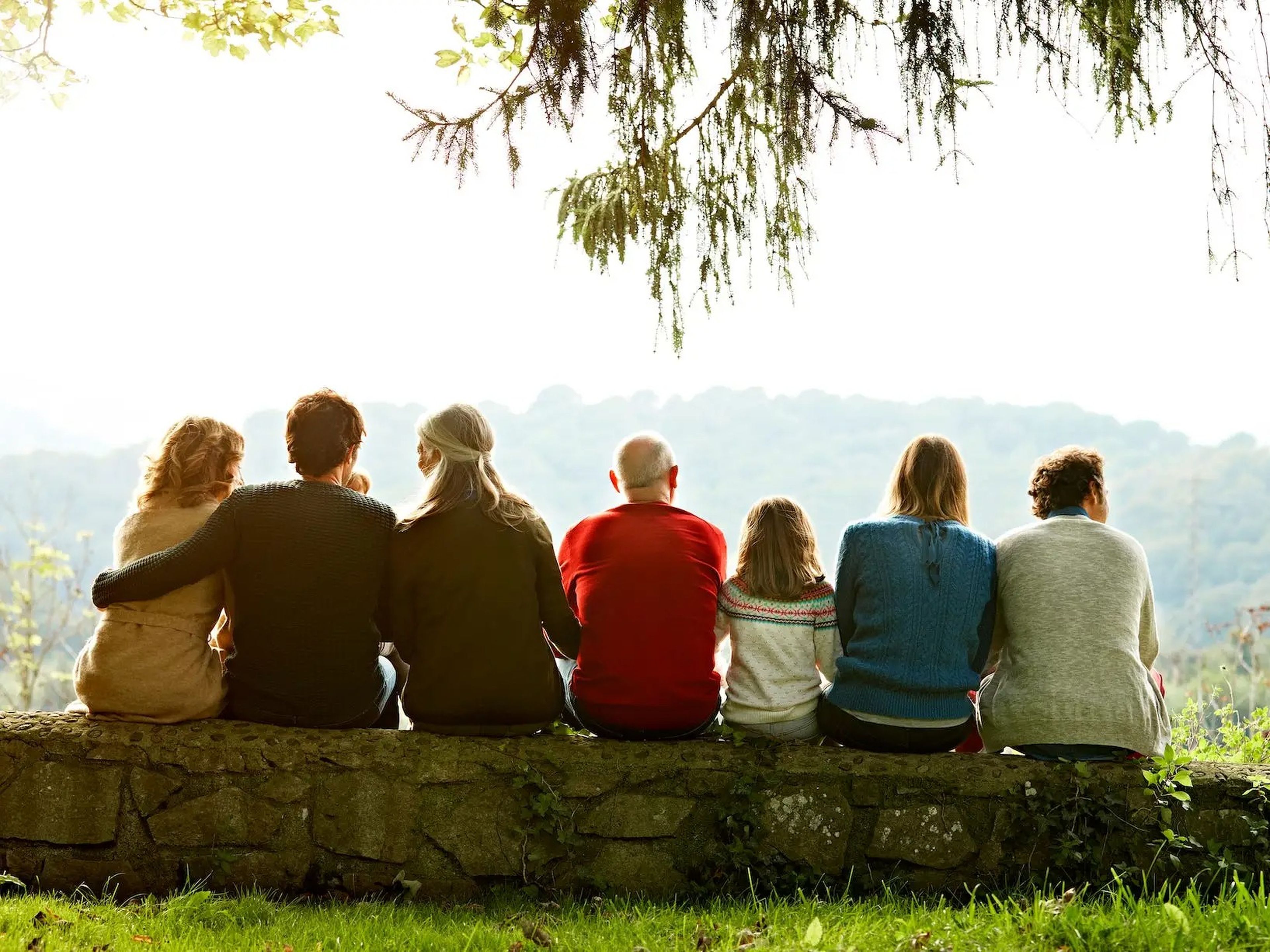 A multigenerational family sitting on a ledge with their arms around each other.