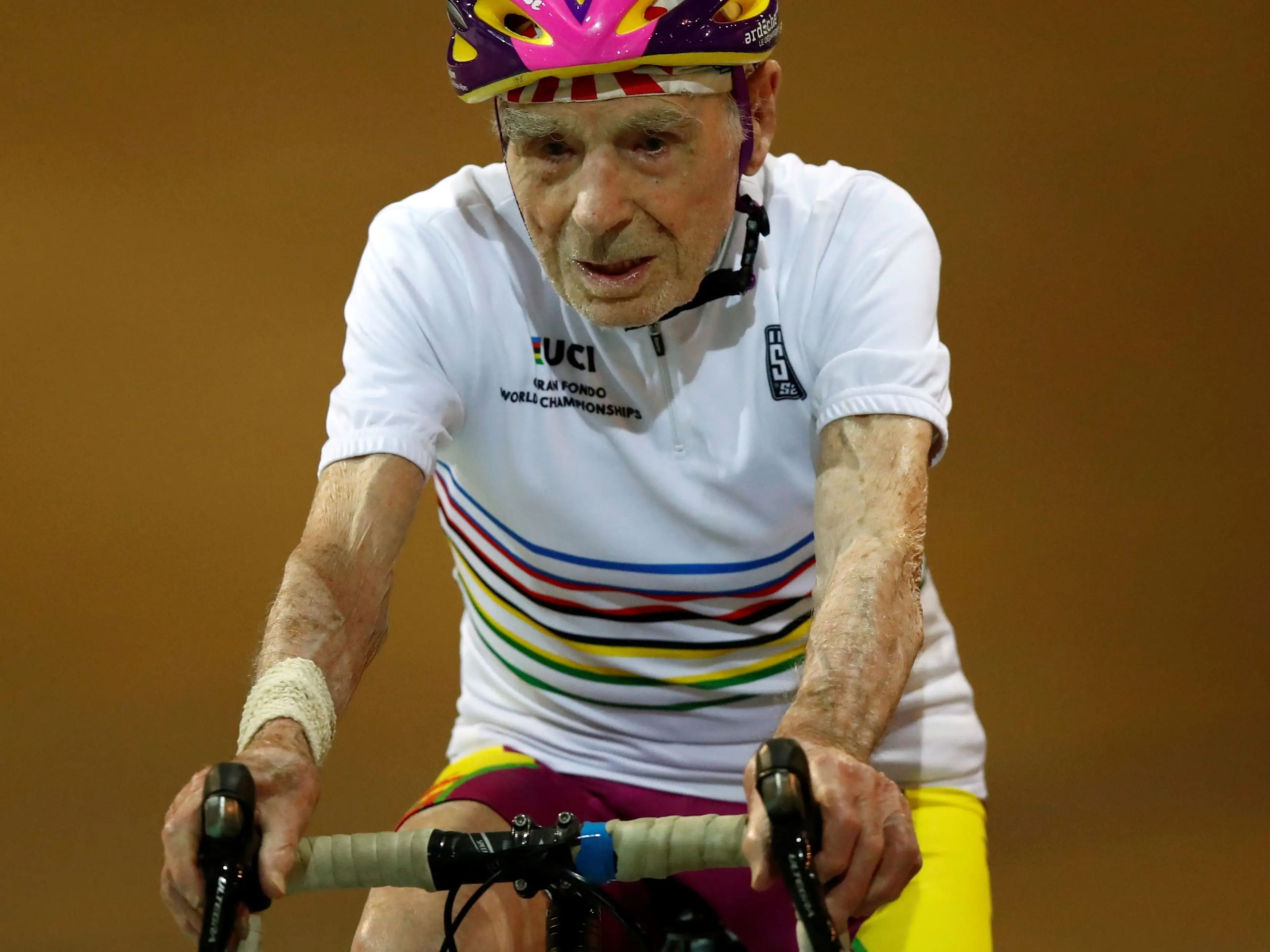 Robert Marchand sitting on a bike while wearing a black and pink bicycle helmet.
