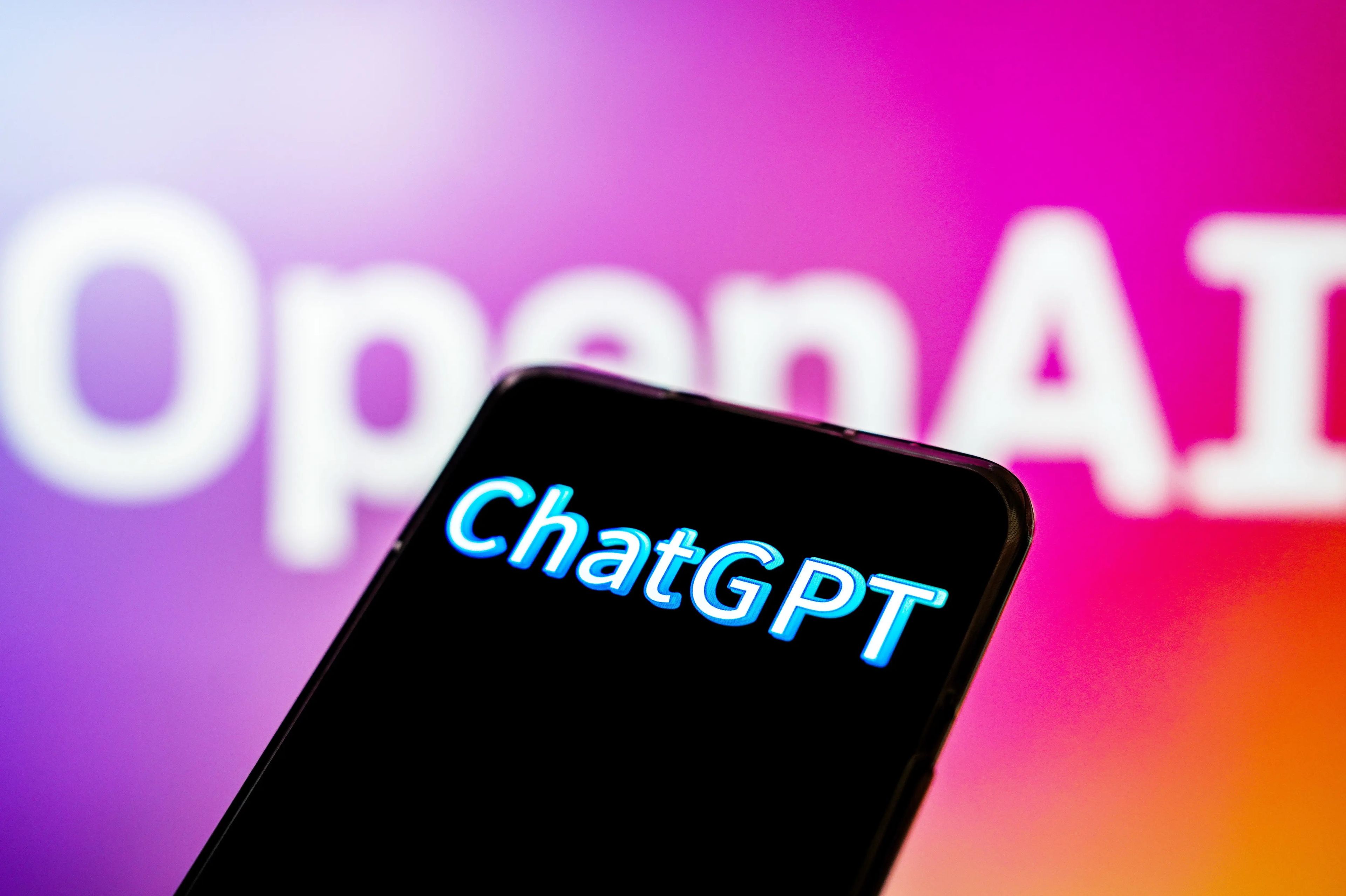 Un logo de ChatGPT en la pantalla de un teléfono móvil frente al logo de OpenAI.