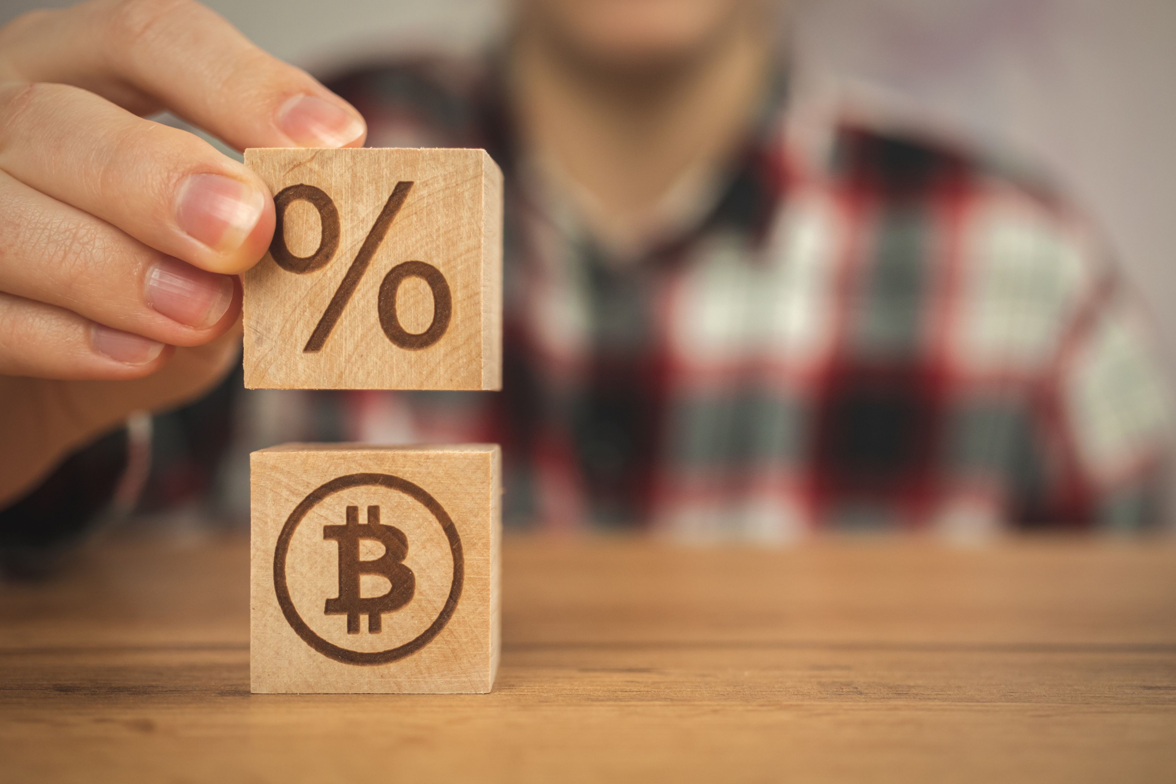 Una persona coloca un dado con el símbolo del porcentaje encima de otro con el de bitcoin. 