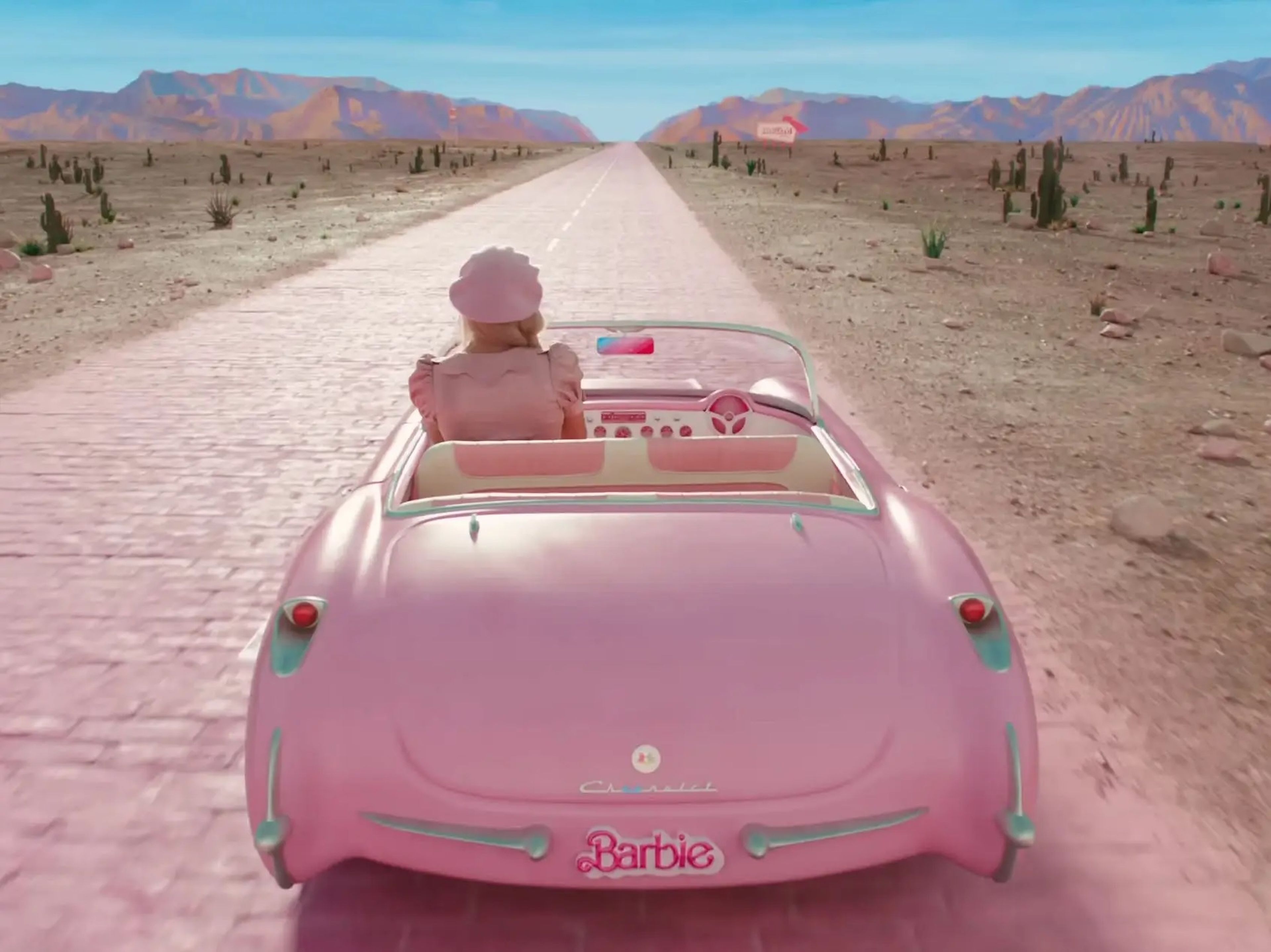 Margot Robbie conduciendo por una carretera de ladrillos rosas.