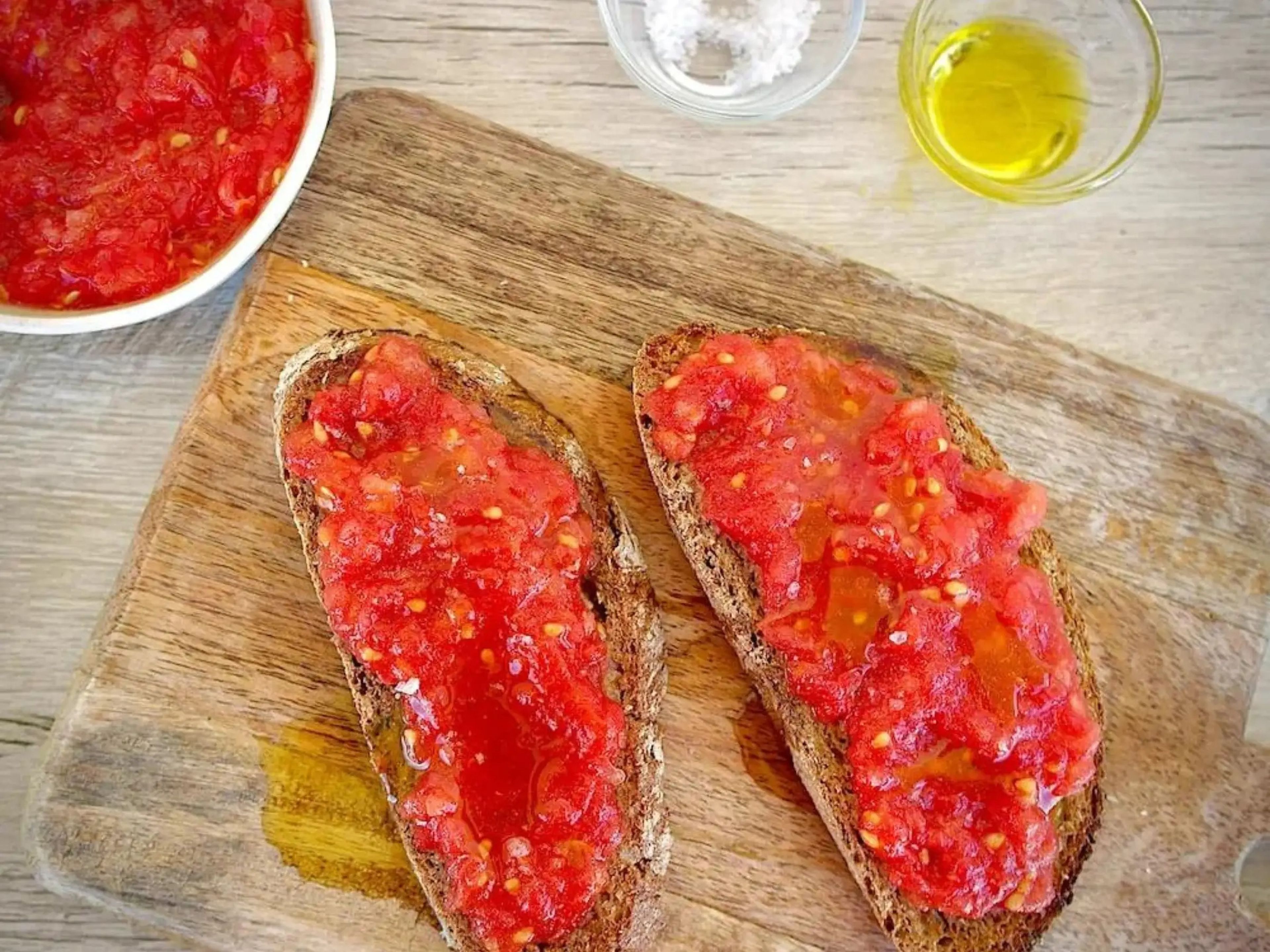 Pan con tomate on a wooden chopping board with bowls of tomato, salt and olive oil