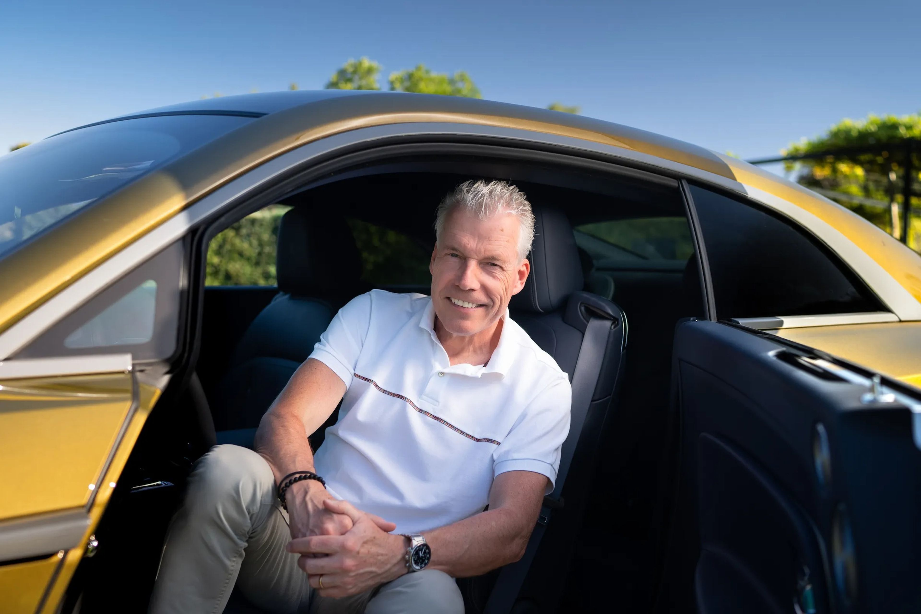 Torsten Müller-Ötvös, CEO de Rolls-Royce, sentado en el asiento delantero de un Rolls-Royce amarillo con la puerta abierta.